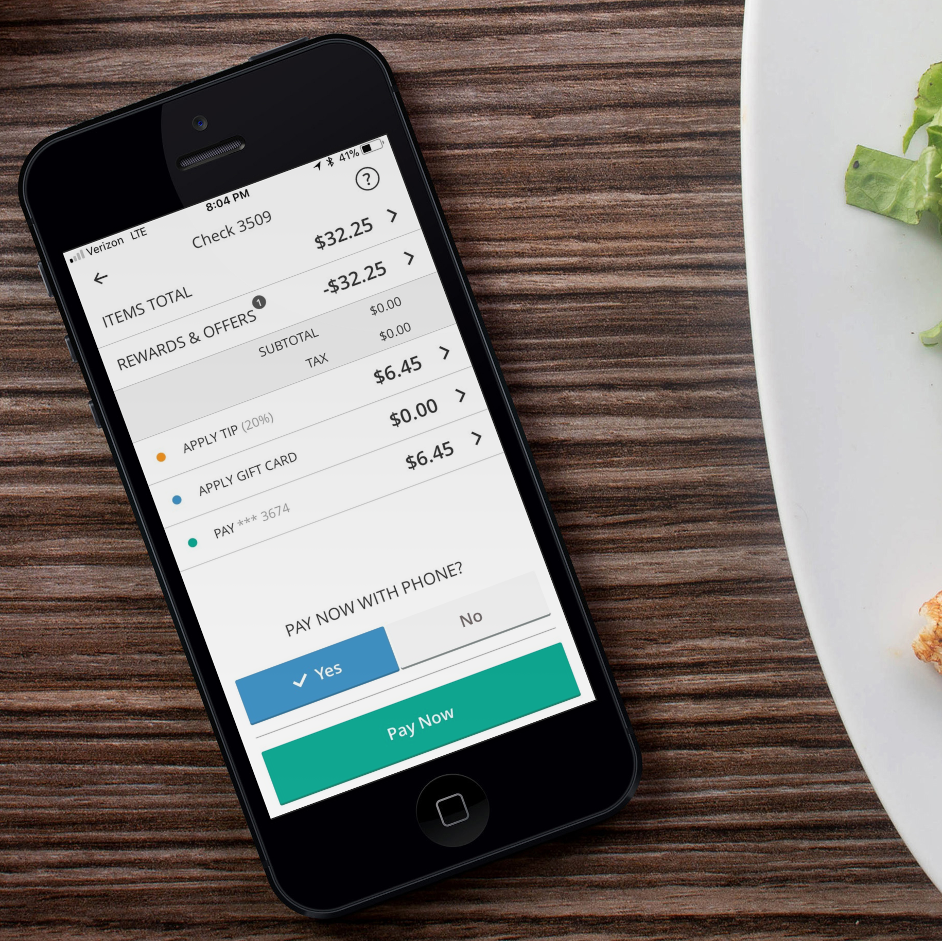 Mobile payment screen showing a receipt for a purchase of $32.25, with options to apply a tip, gift card, and pay with a phone, on a wooden table next to a white plate with some greens.