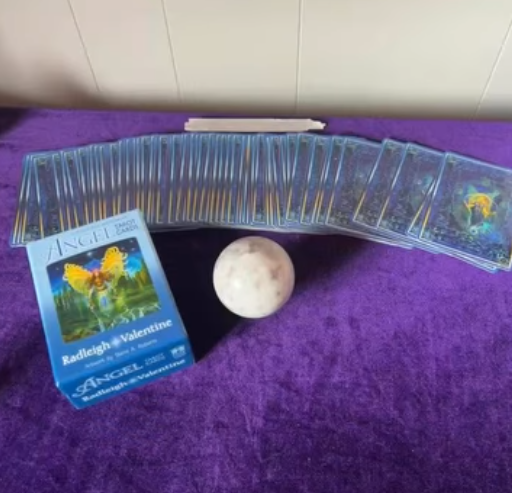 Tarot cards, a moon figurine, and a card titled 'Angel Oracle: Radiate Love & Valentine' on a purple cloth.