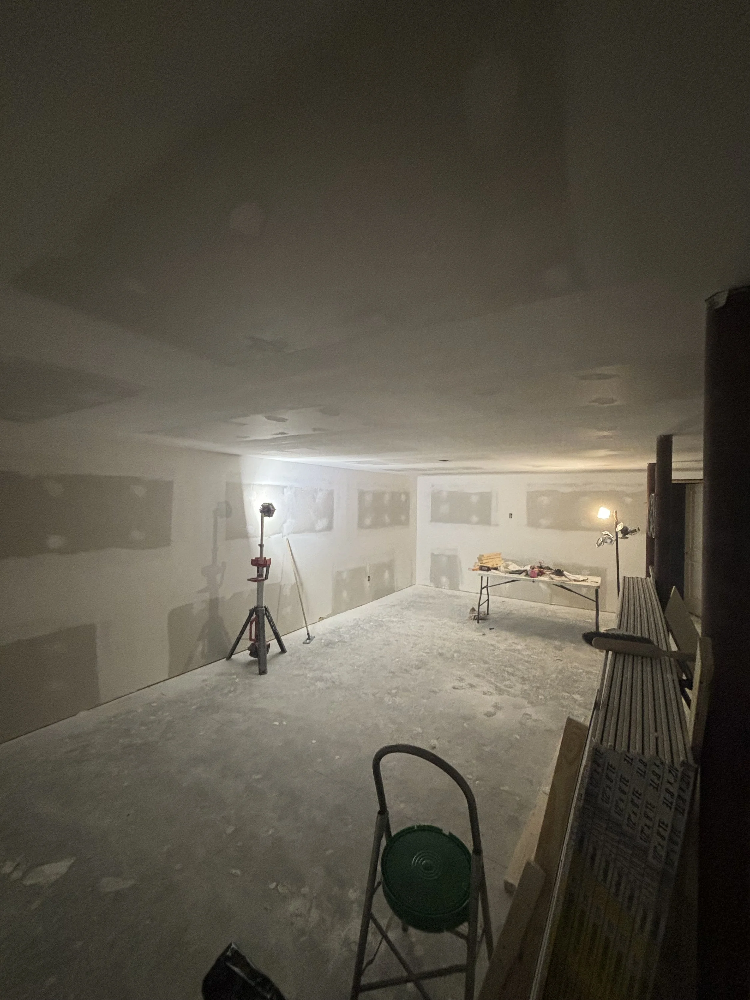 Unfinished room under construction with drywall walls, construction lights, and workbenches.