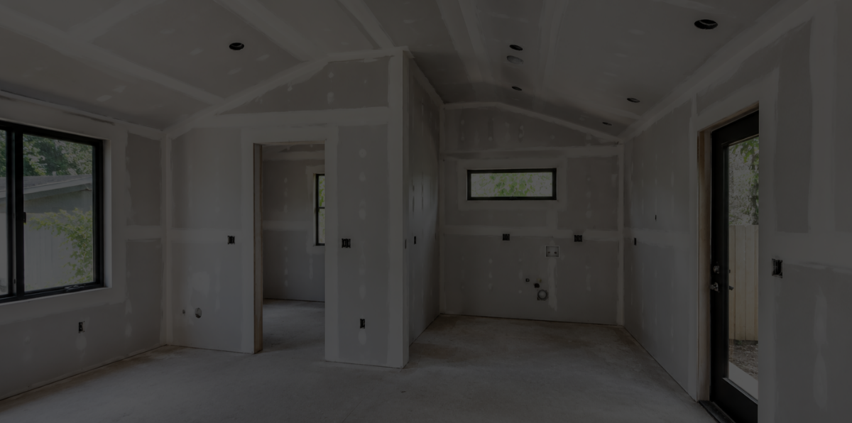 Unfinished room in a house under construction with drywall installed, electrical outlets, windows, and a door.