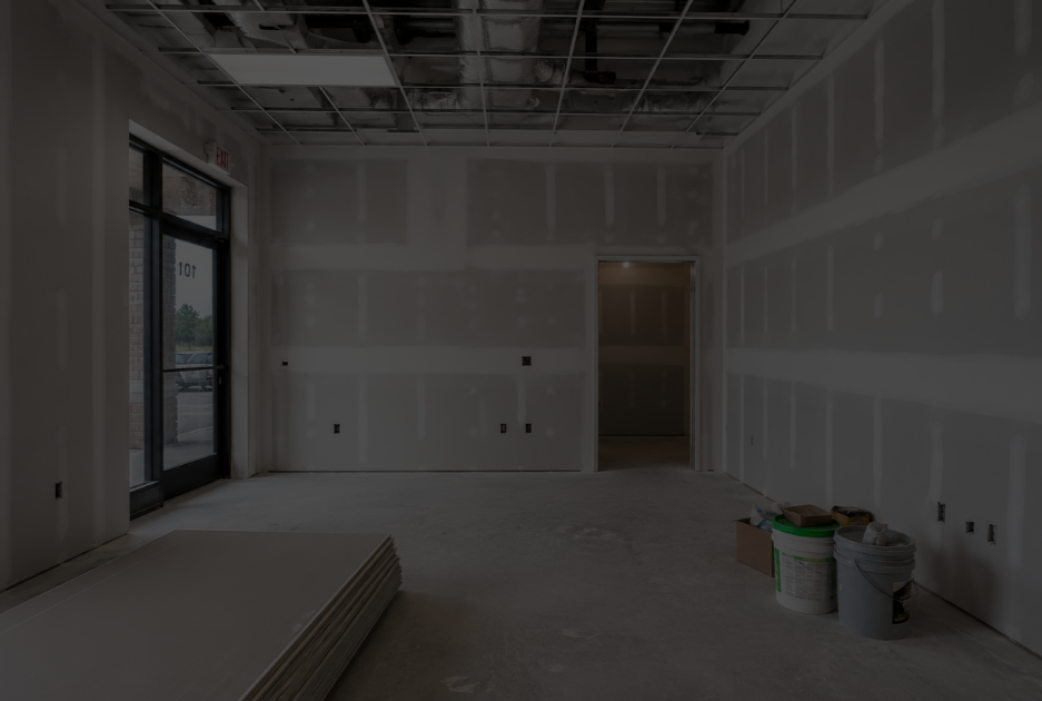 Interior of a construction site room with drywall installed, construction supplies on the floor, and an unfinished ceiling.