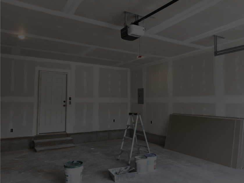 An unfinished garage with drywall walls, a ladder, buckets of paint, and a garage door opener installed on the ceiling.