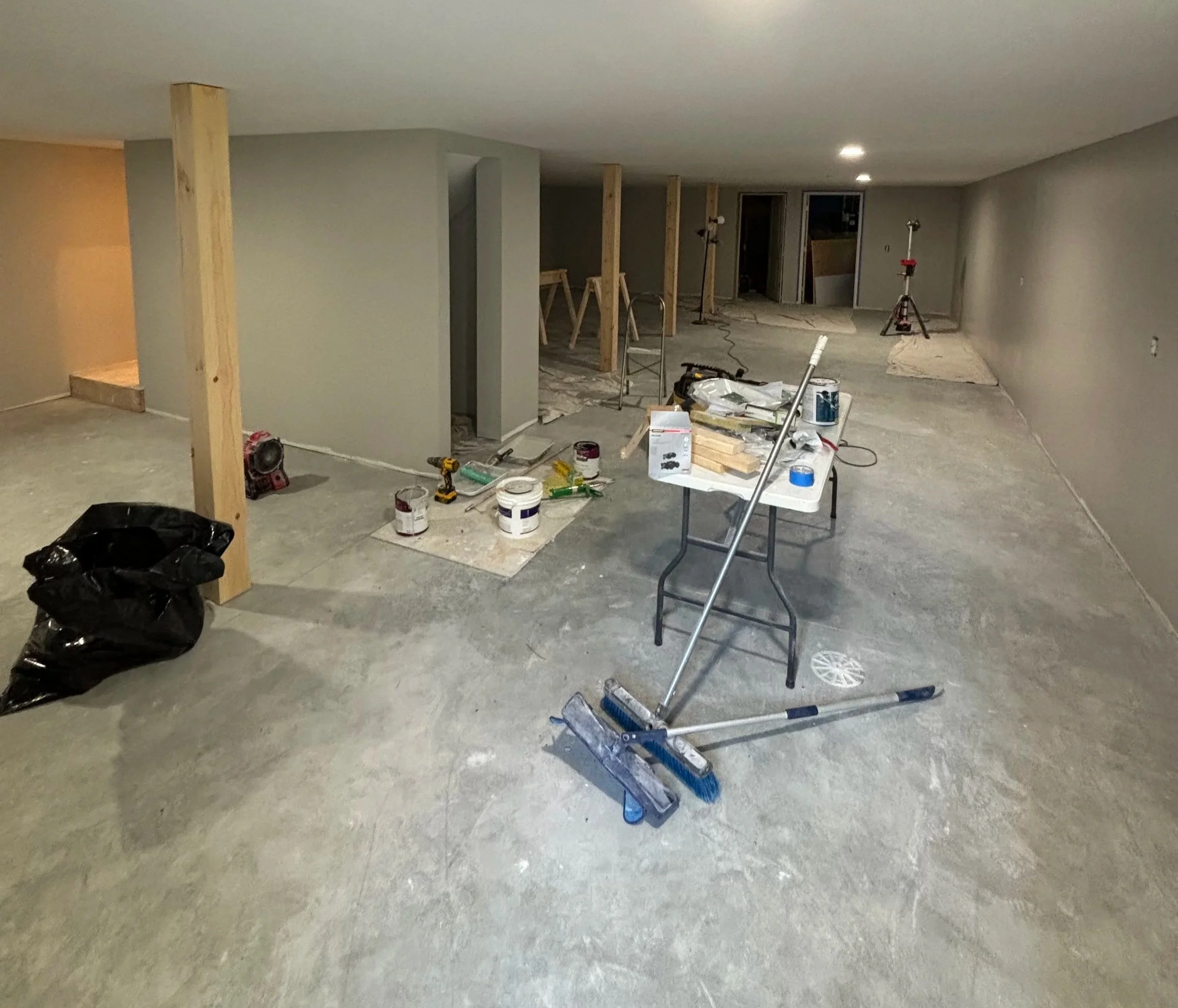 Interior of a room under construction with scattered tools, paint cans, a ladder, and wooden support beams.