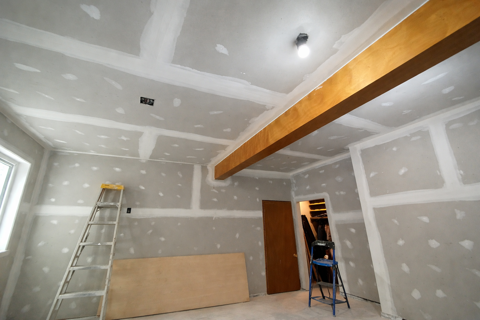 Room under construction with drywall and joint compound, ladder, wooden beam, and an open closet.