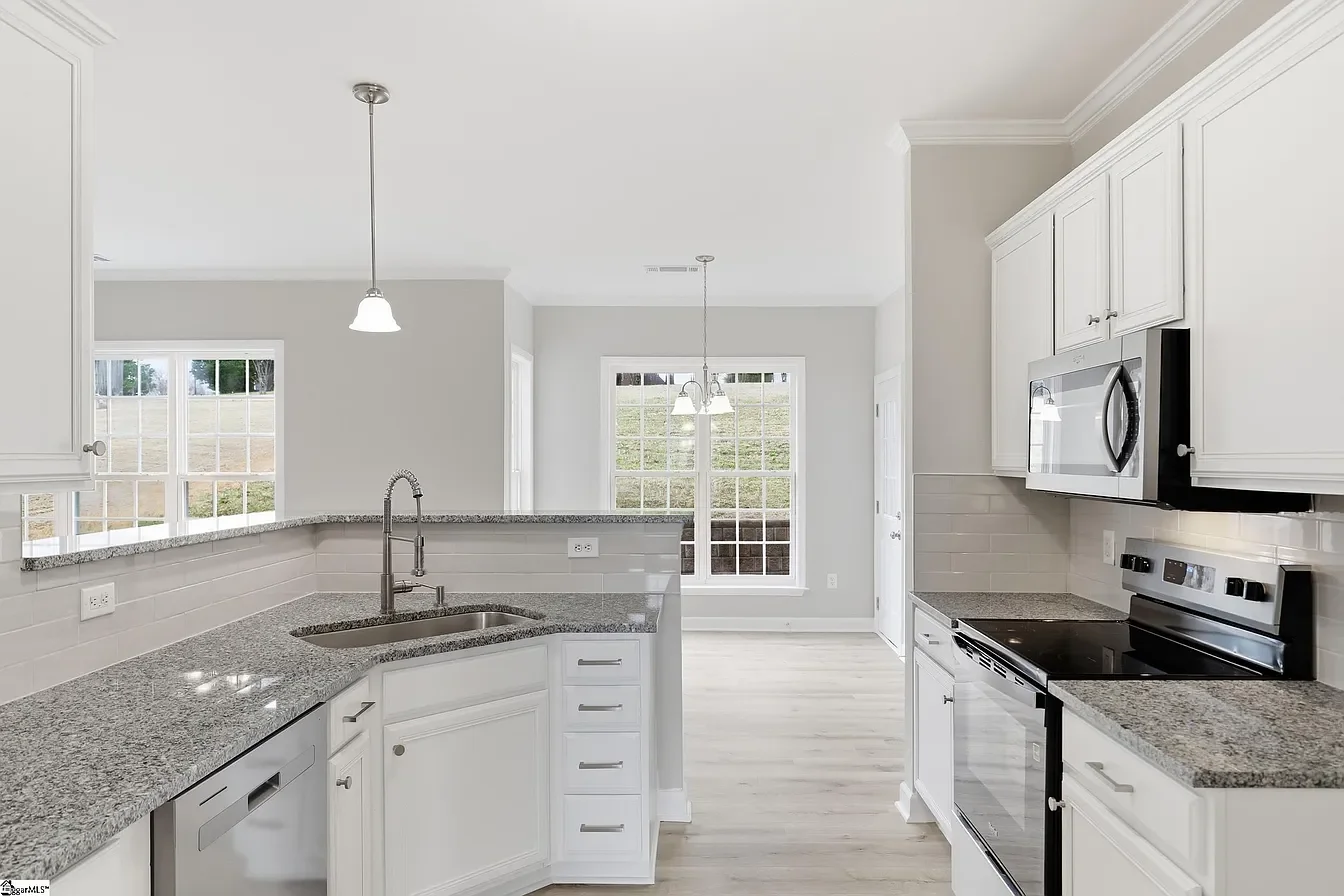 Modern kitchen with granite countertops, white cabinets, stainless steel appliances, large windows, and pendant lighting.
