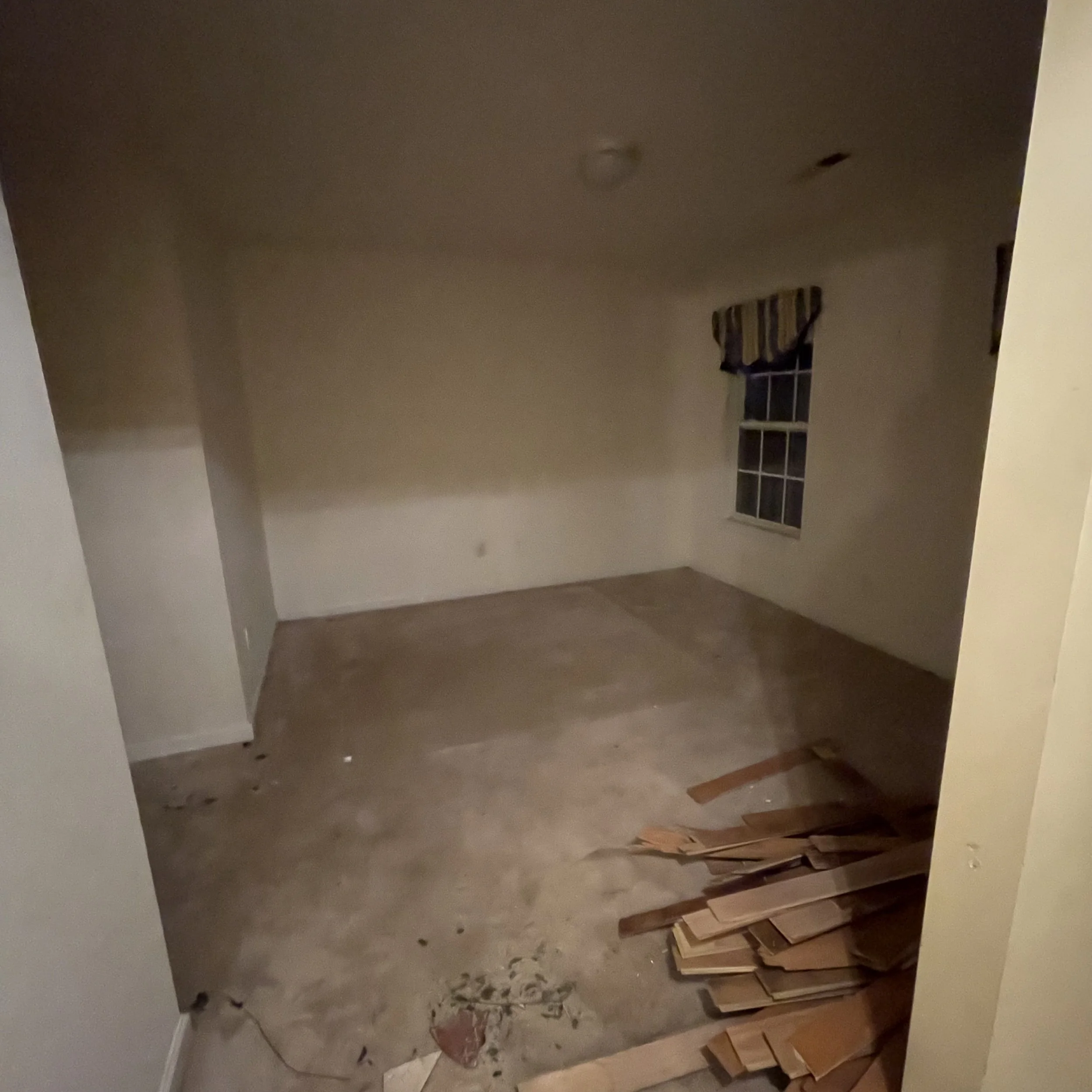 A room under renovation with drywall, construction debris, and stacks of wooden flooring planks.