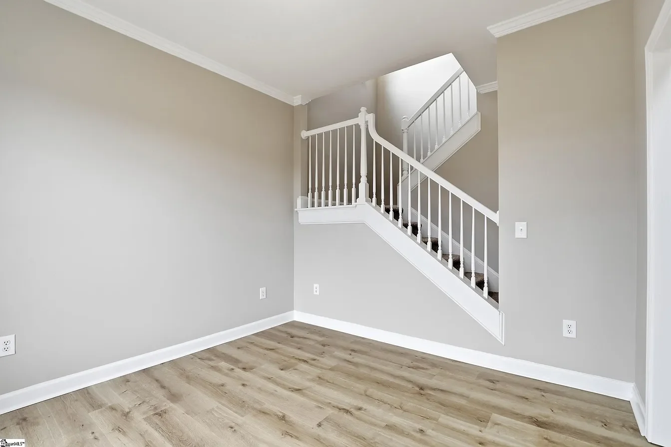 Empty room with light-colored hardwood floors, gray walls, and a staircase with white railing and dark stairs, leading upstairs.