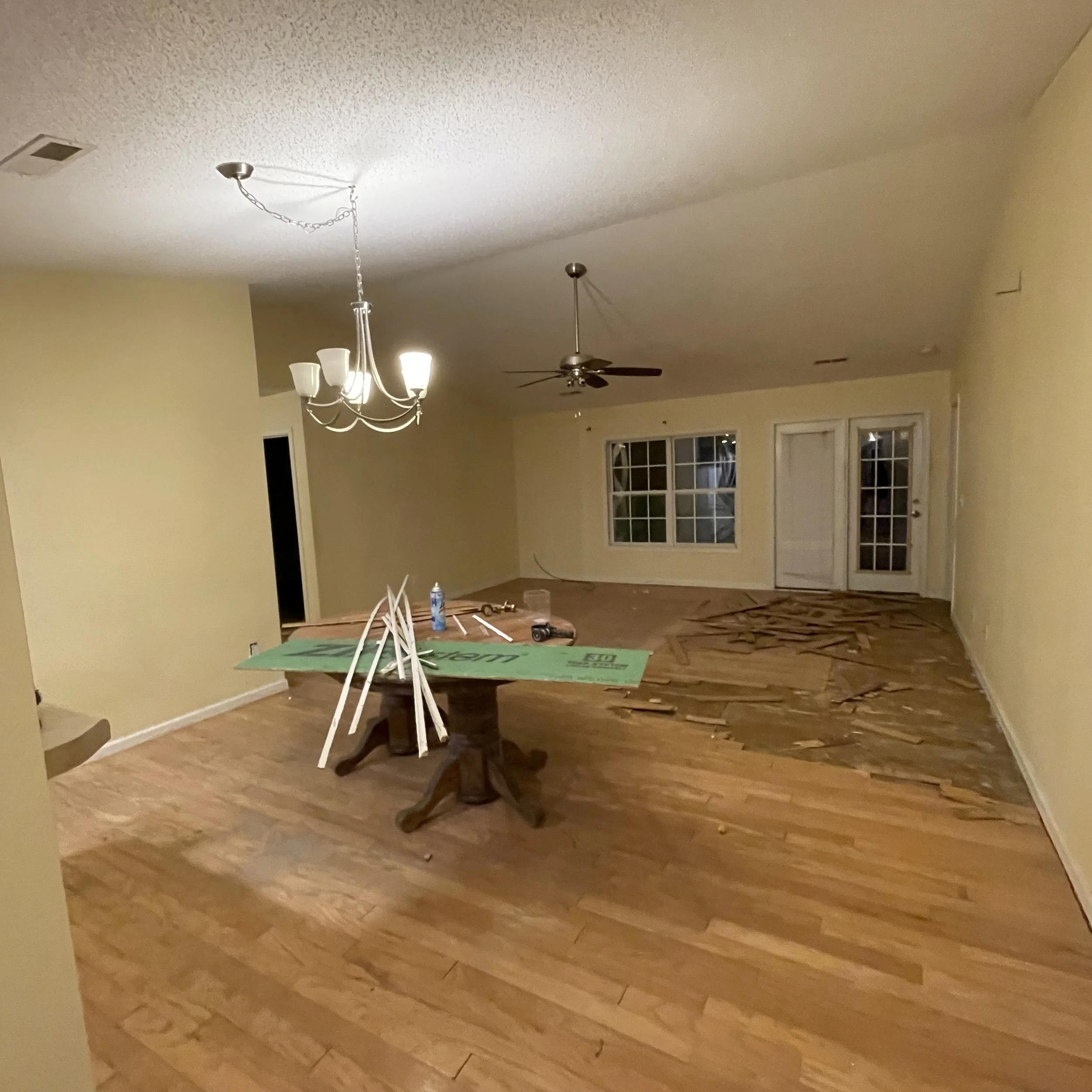 Empty living room with a dining table, hanging light fixture, ceiling fan, and French doors.