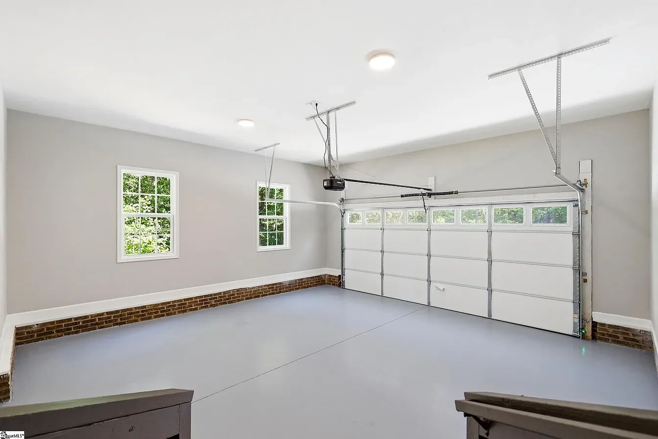 Empty two-car garage with white walls, windows, and a closed garage door, brick details at the base, and ceiling lights.