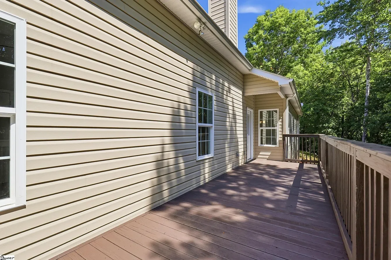 Wooden deck with beige vinyl siding house exterior and surrounding trees