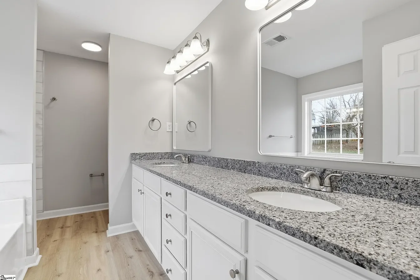 Bathroom vanity with granite countertop, oval sink, large mirror, white cabinets, window, and light fixture.