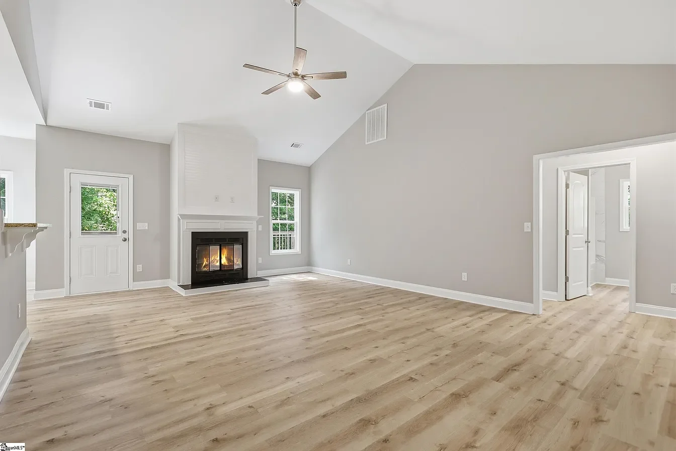 Empty living room with light wood flooring, fireplace, ceiling fan, and neutral-colored walls.