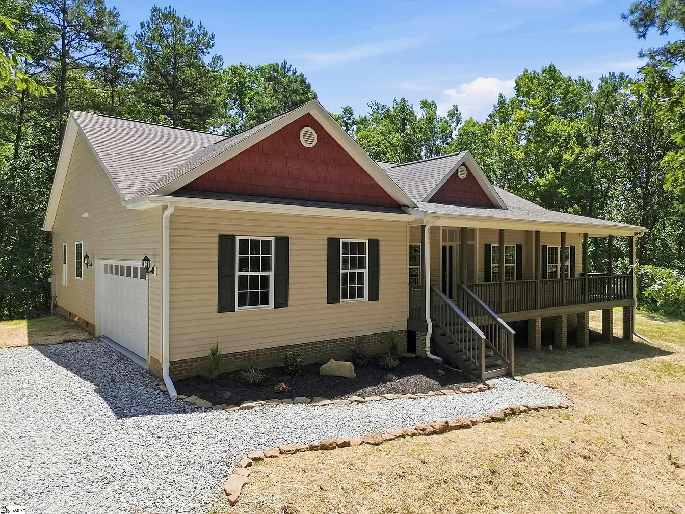 Newly built house with a front porch, surrounded by green trees under a partly cloudy sky.