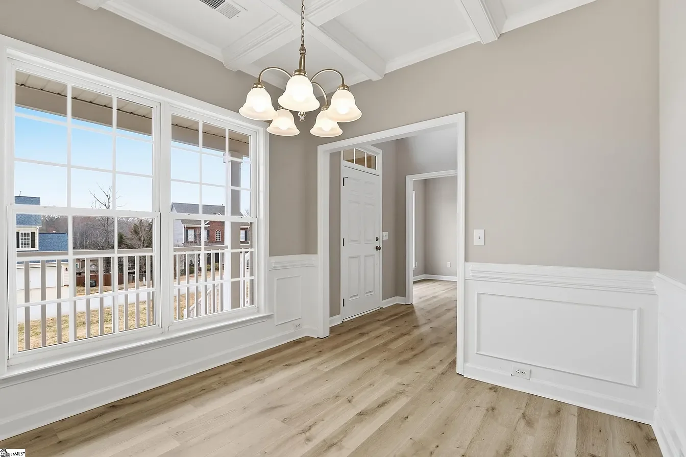 Empty dining room with large windows, a chandelier, beige walls, and light hardwood floors.