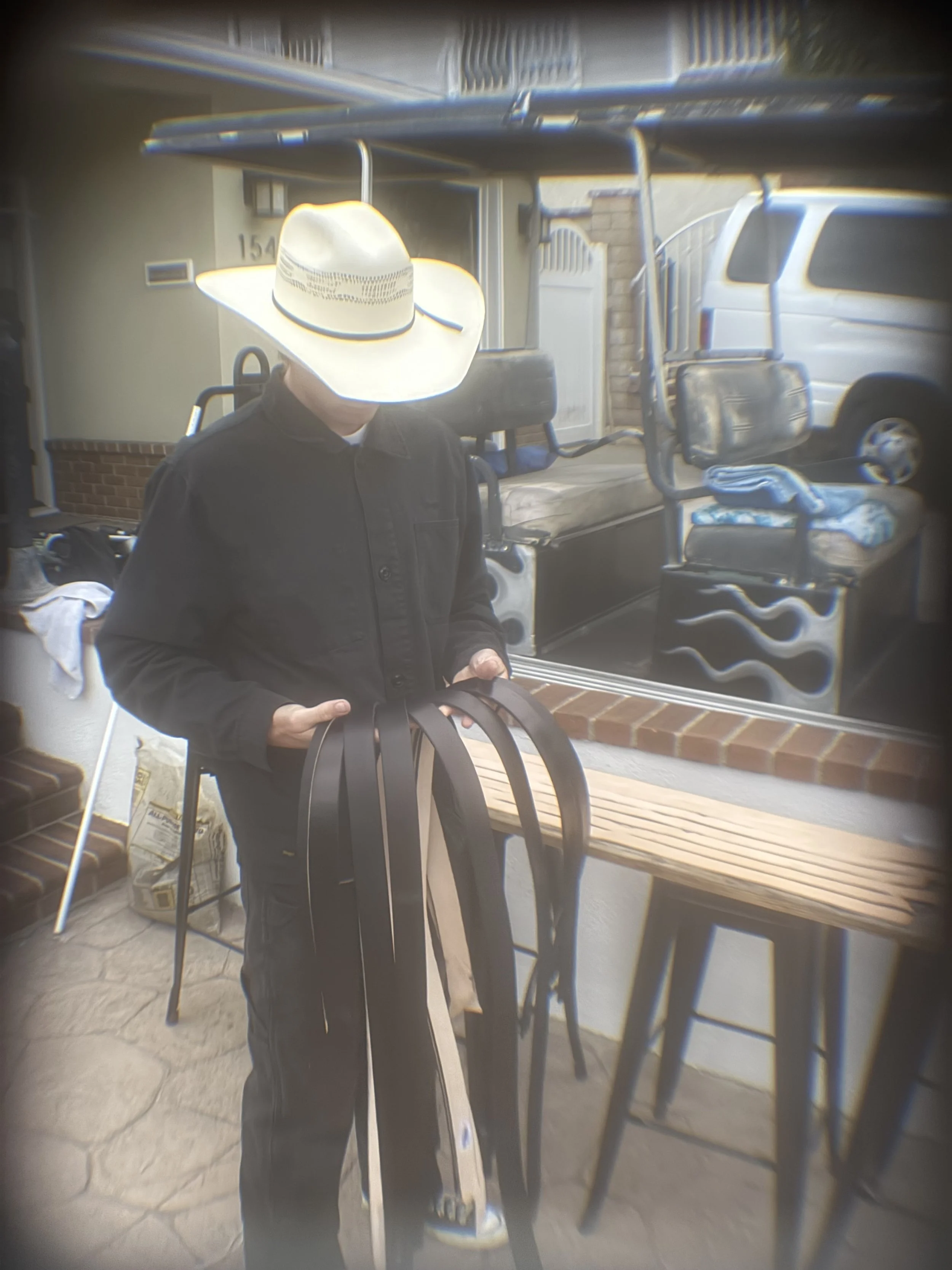 Person wearing a large white cowboy hat, black jacket, and black pants holding several black and white folding chairs indoors with a brick countertop, wooden bench, and a window reflecting outdoor cars.