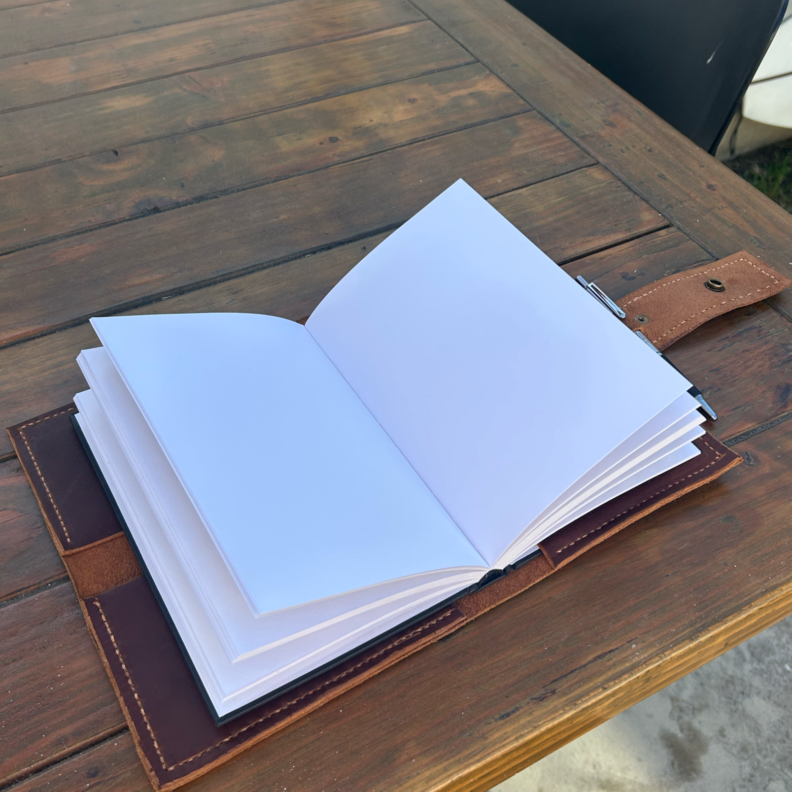 Open blank white notebook with leather cover on wooden table.