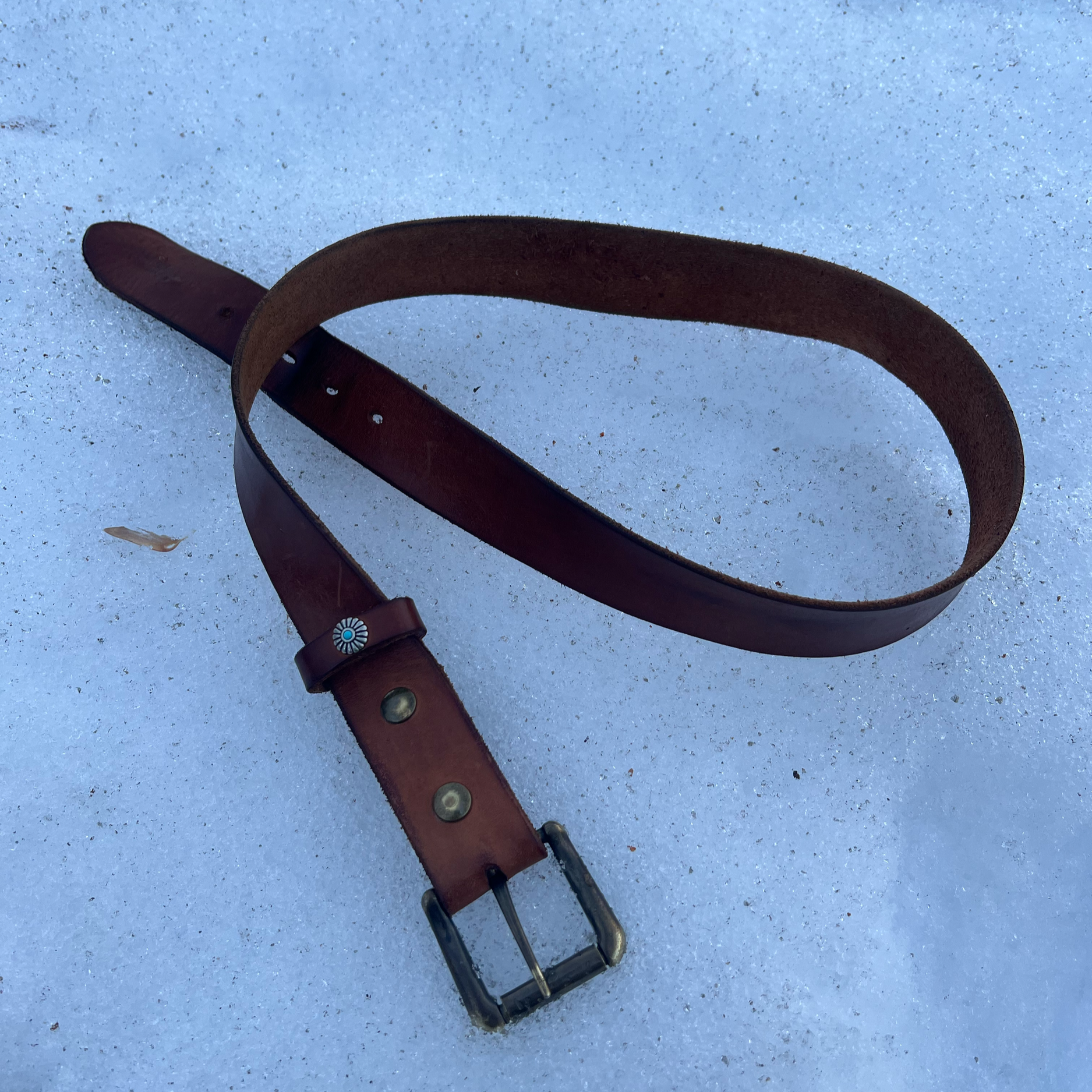 A brown leather belt with a silver buckle lying on snow.