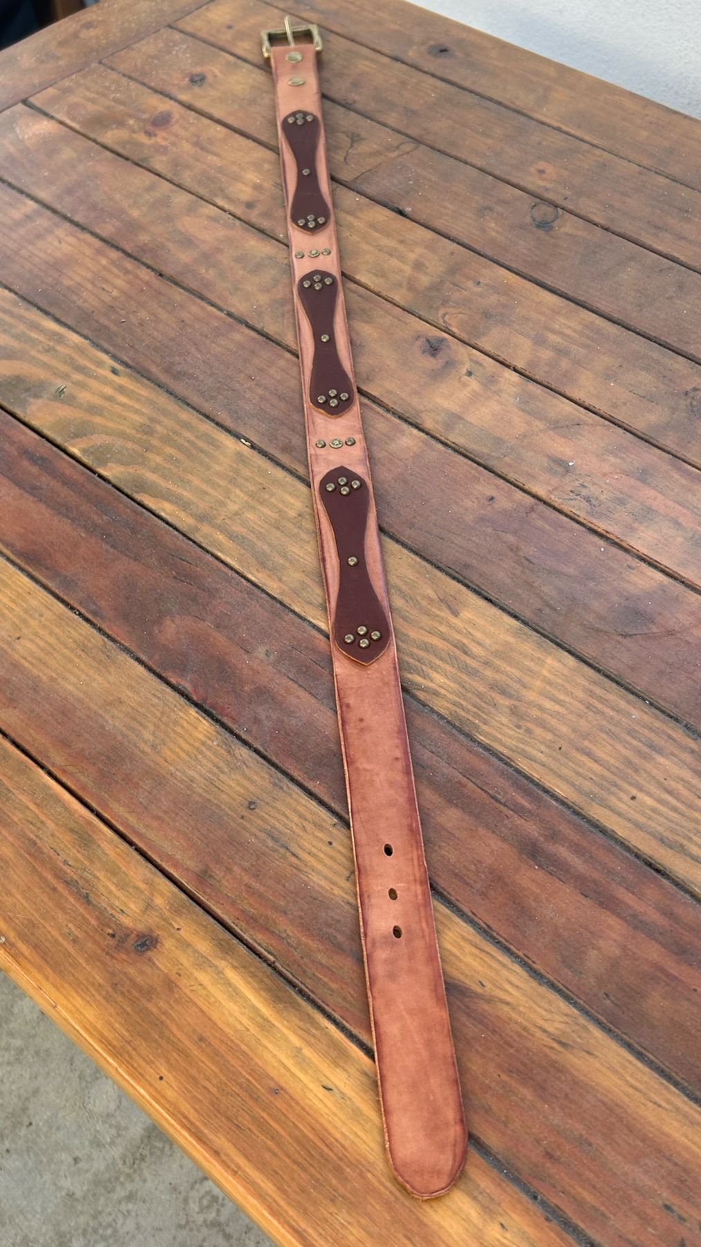 A brown leather belt with a brass buckle lying on a wooden surface.