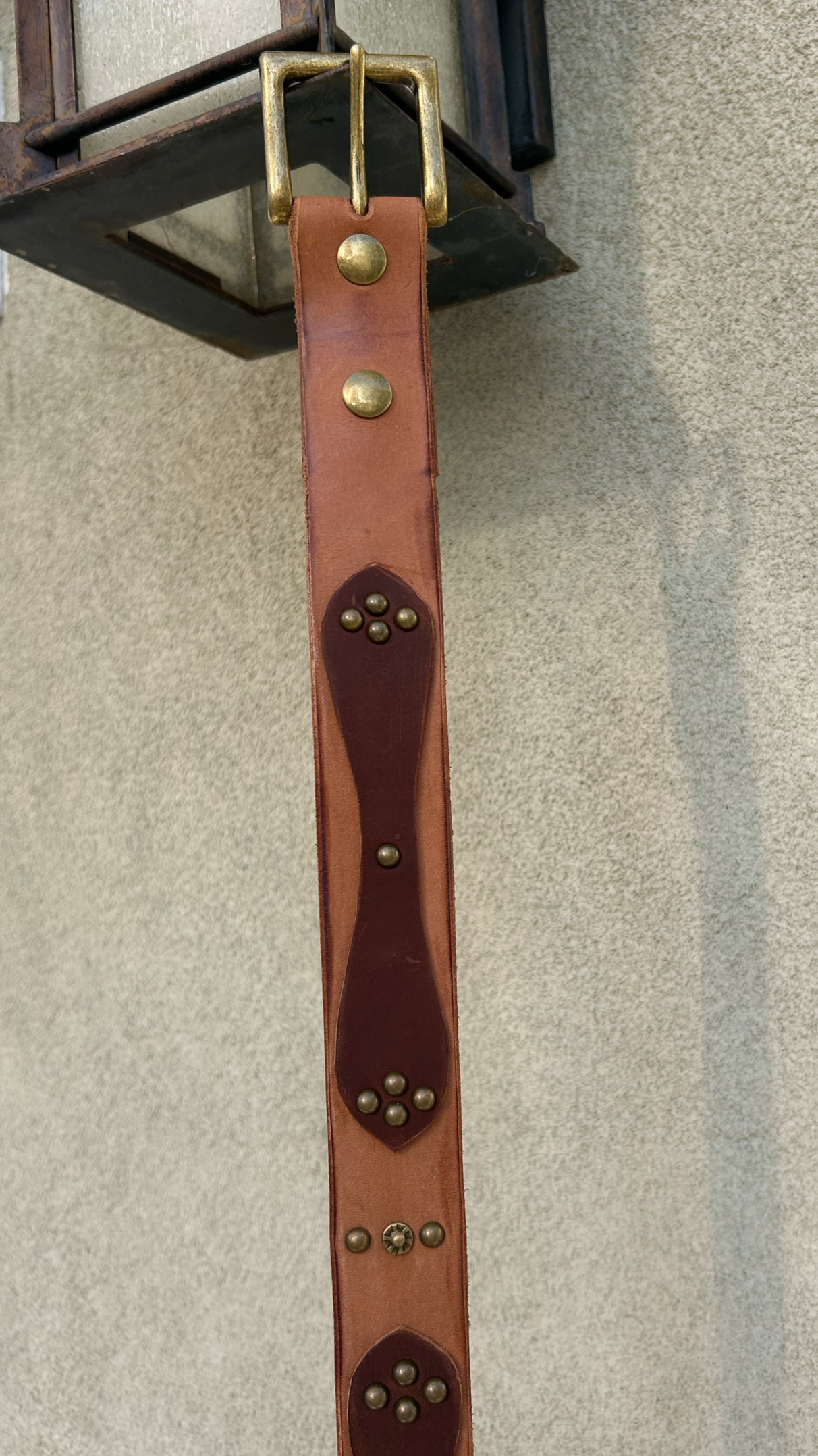 A leather strap with metal studs hanging from a metal frame attached to a wall.