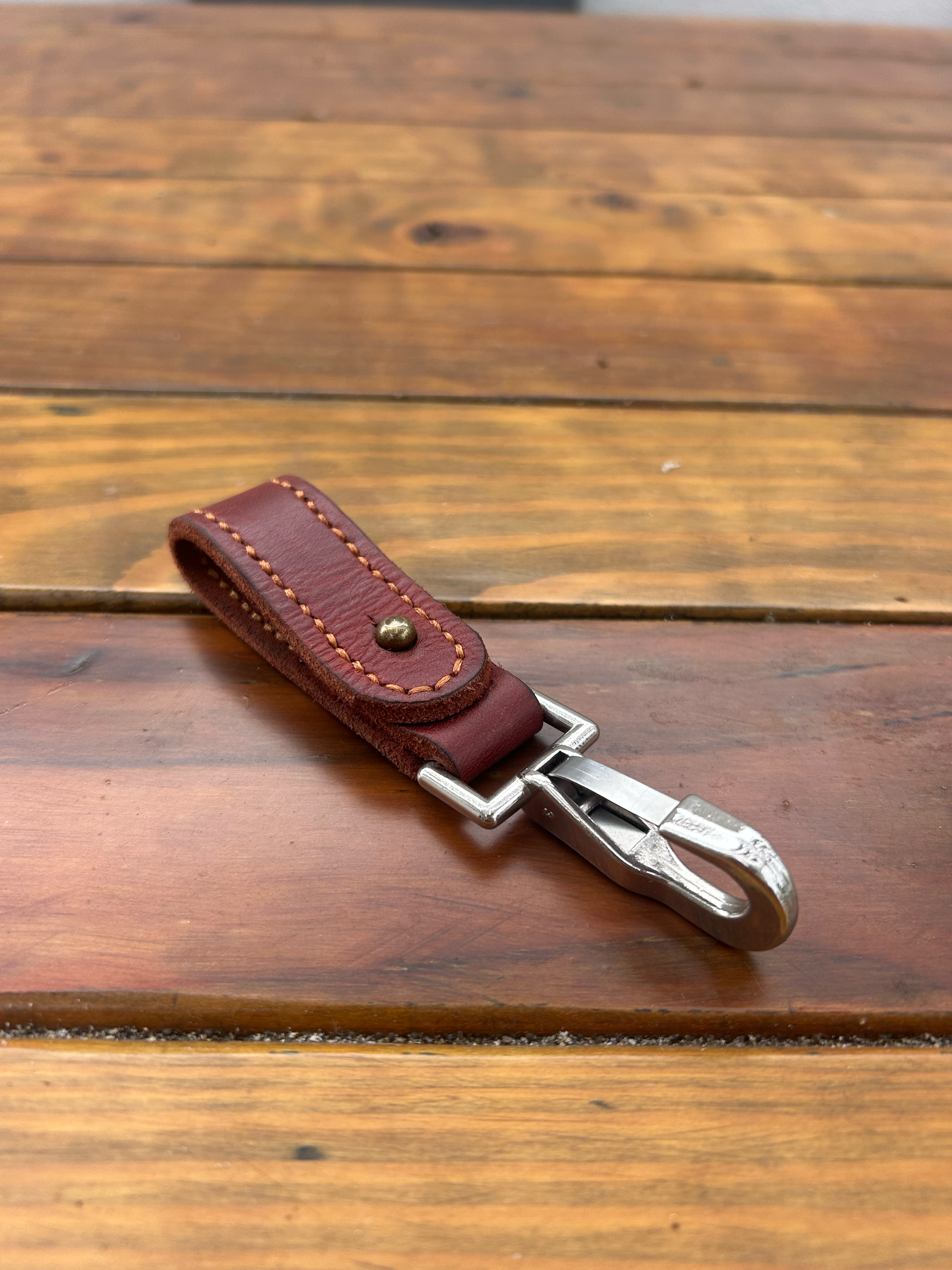 A leather keychain with a metal hook on a wooden surface.
