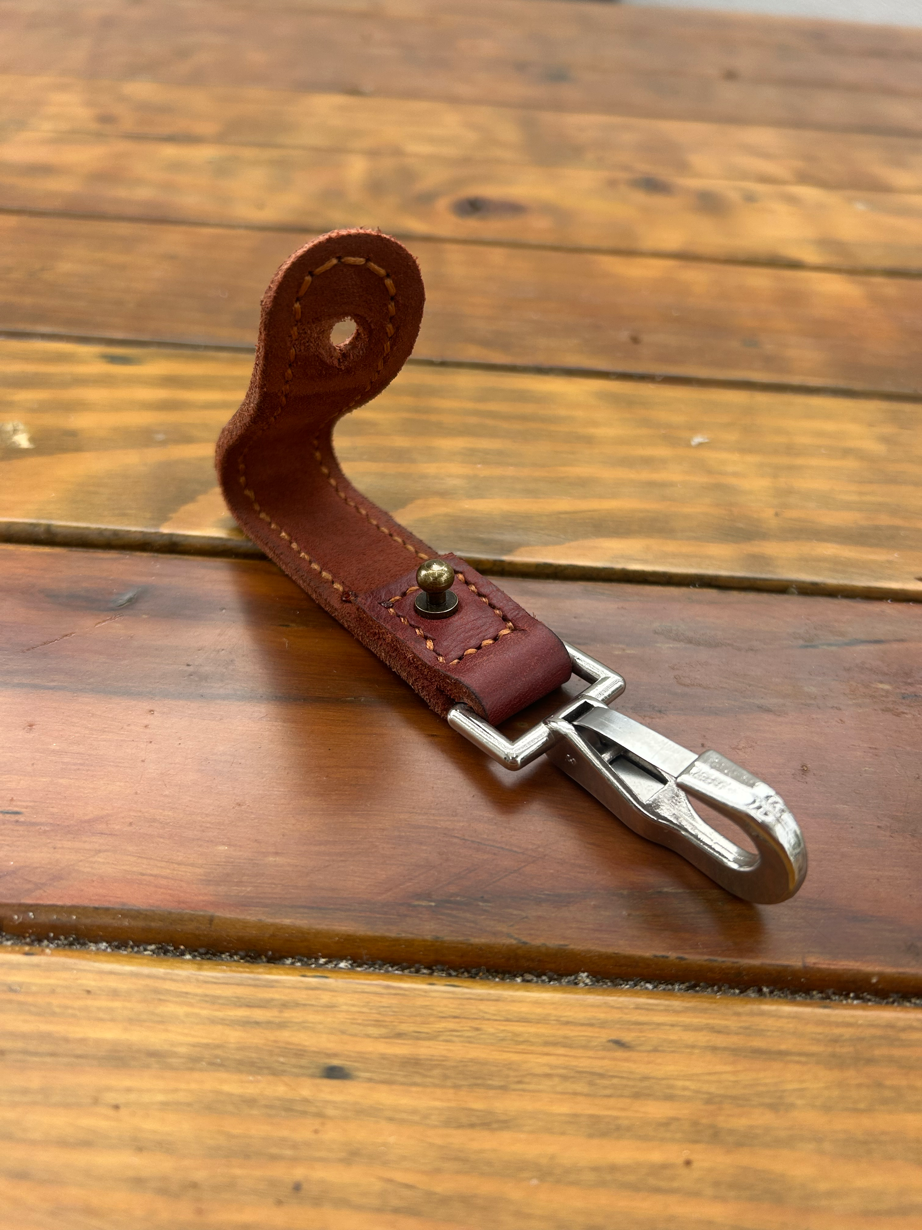 A leather keychain with a metal clip on a wooden surface.