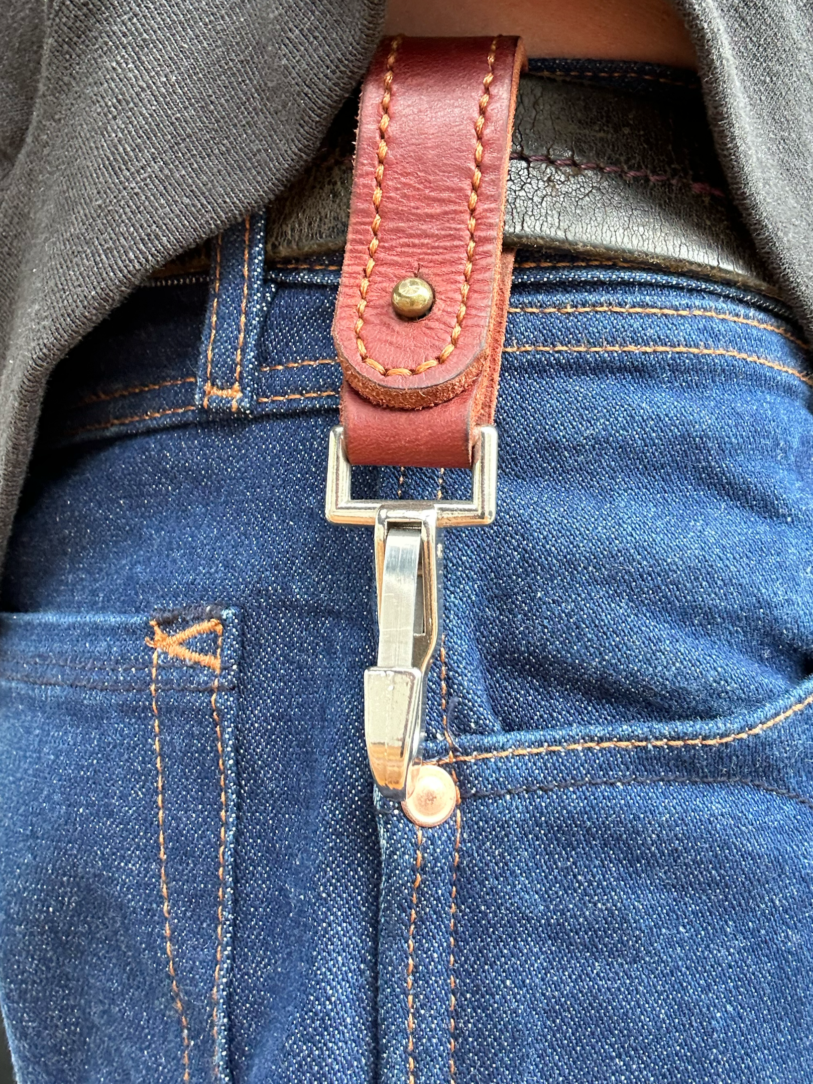 Close-up of a person wearing blue jeans with a brown leather belt with a silver hook.