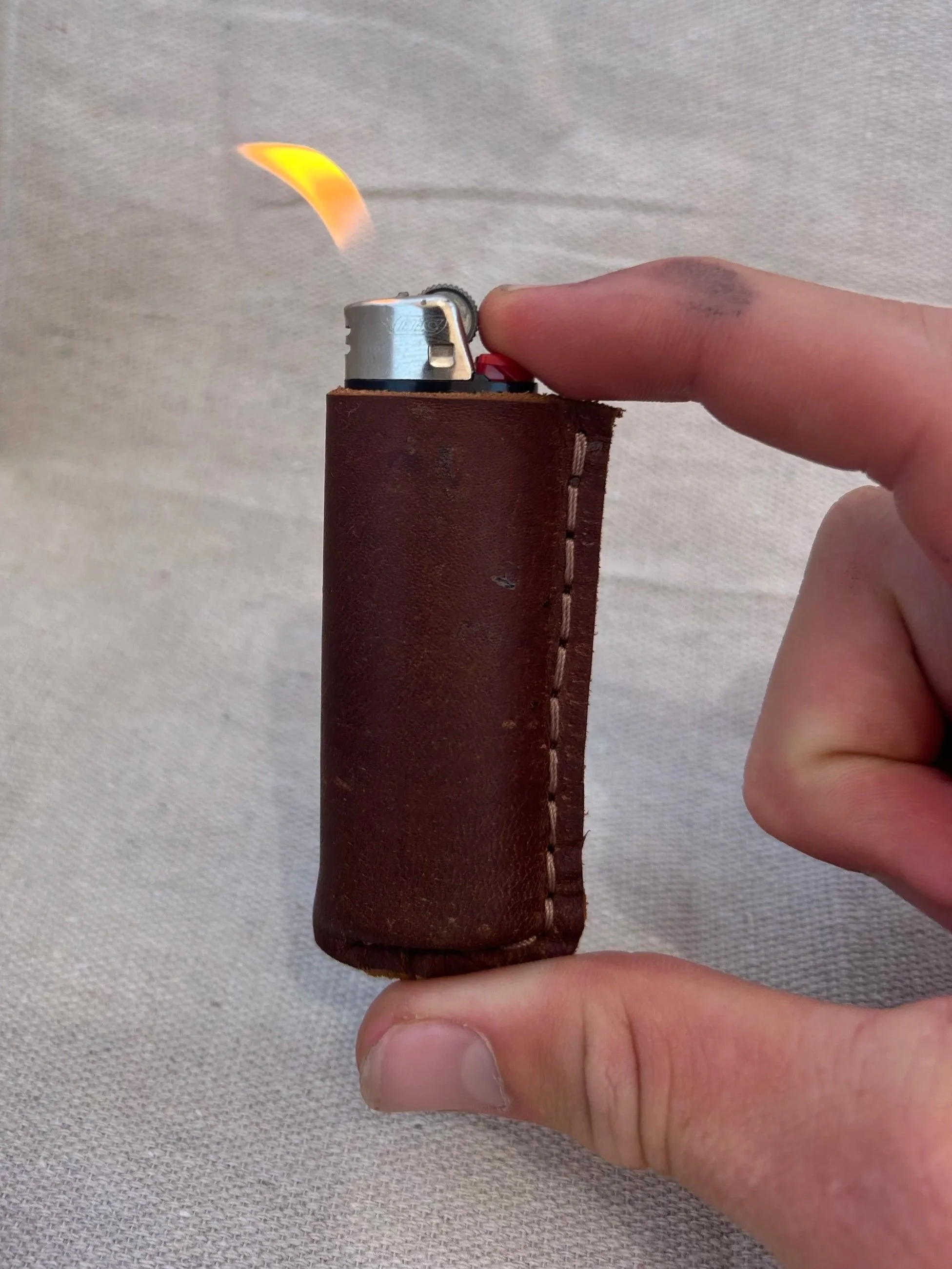 A hand holding a lighter wrapped in a brown leather case with the flame ignited.