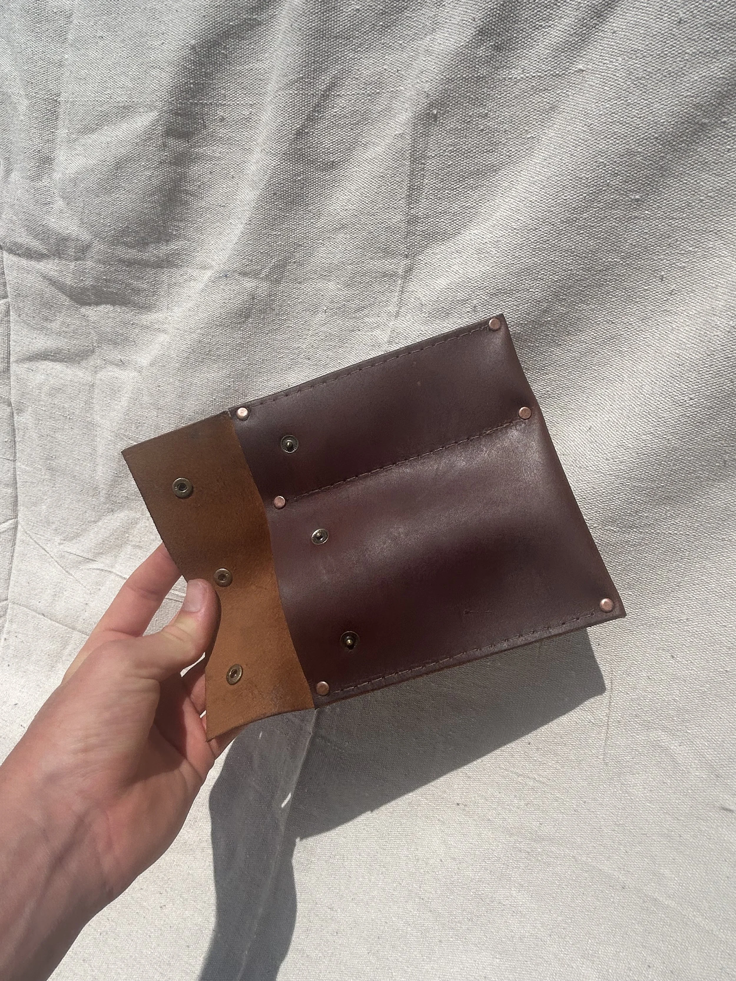 A hand holding a small, rectangular leather wallet with a multicolored design, featuring brown shades and metal rivets, against a light, textured fabric background.