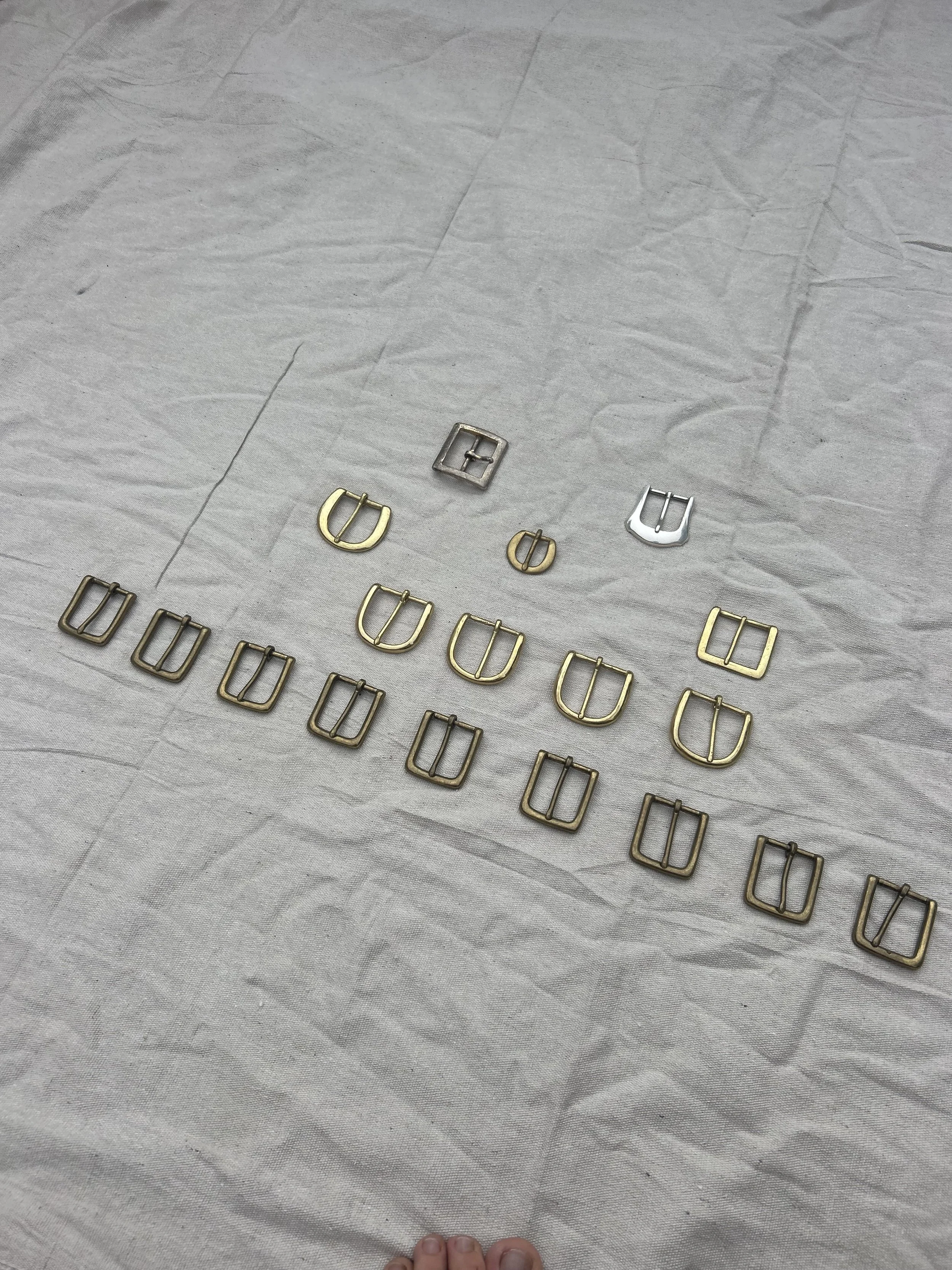 A collection of metal buckles in different shapes and sizes, arranged on a white textured surface.
