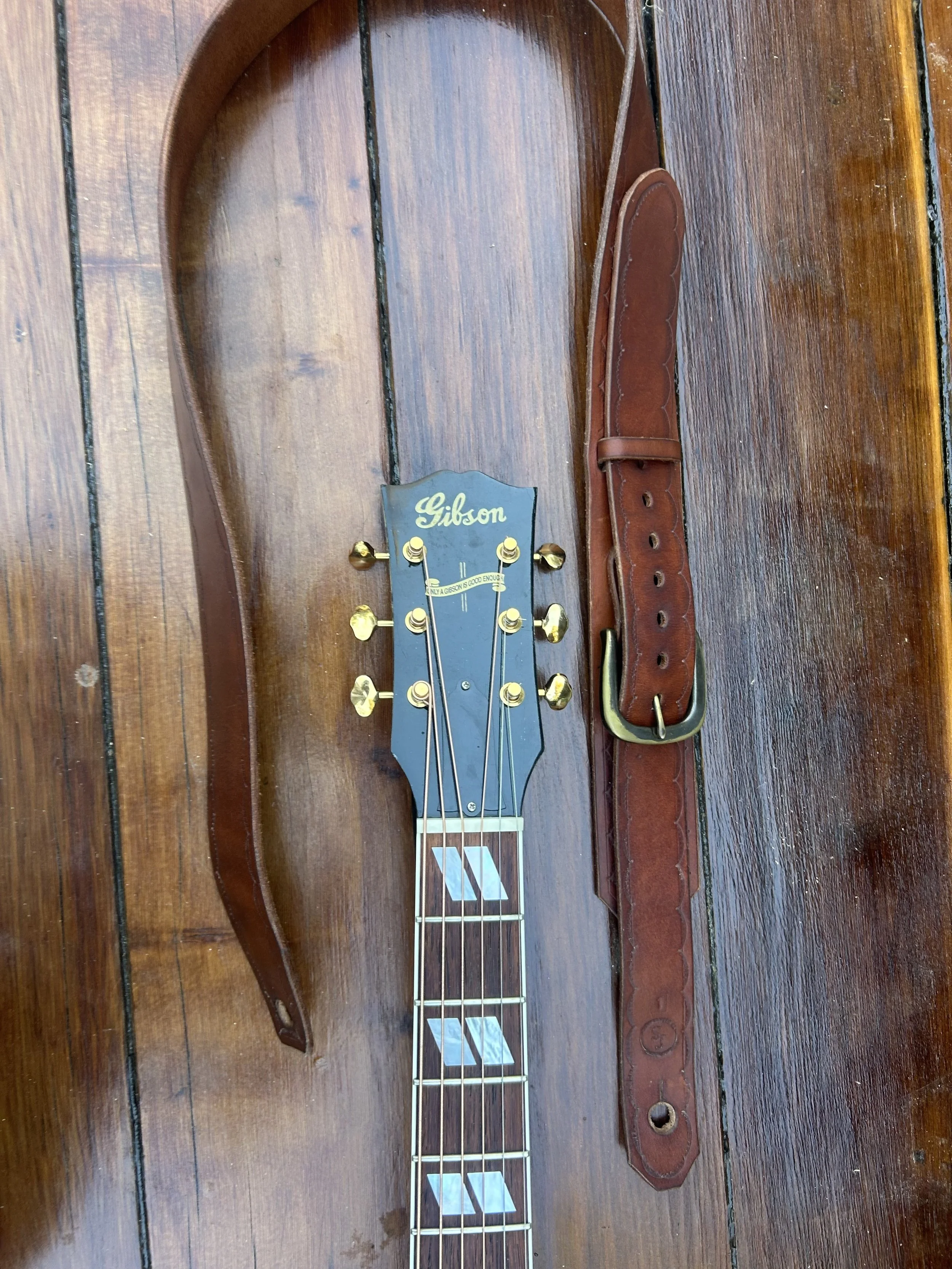 Gibson guitar headstock with a guitar strap and case laid out on a wooden surface.