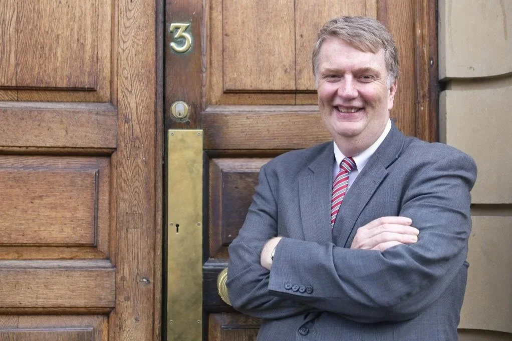 Rev. Dr. David Wikinson standing in front of a door with is arms crossed.