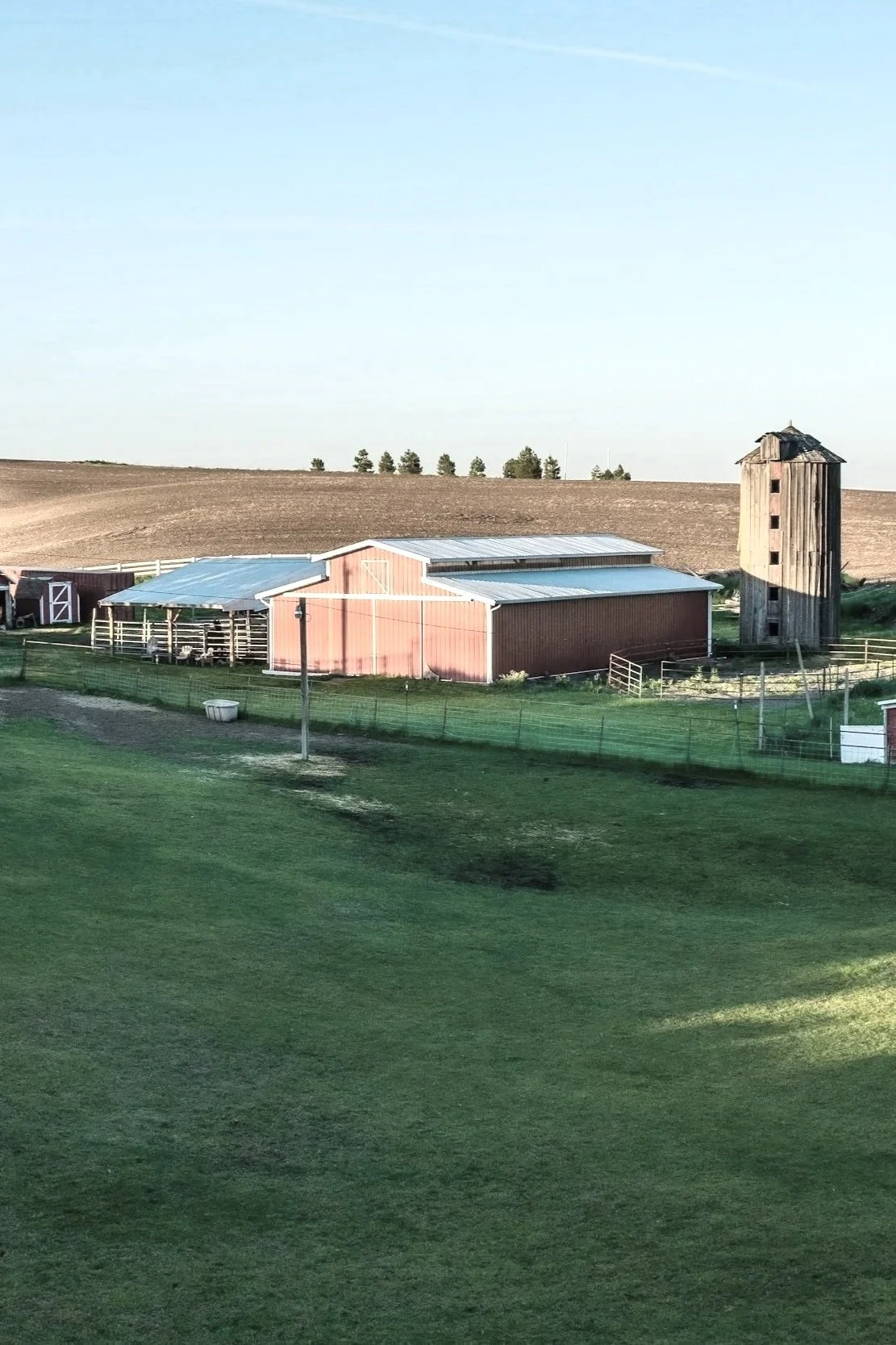A farm scene with a red barn, a wooden silo, a grassy field, and clear sky in the background.