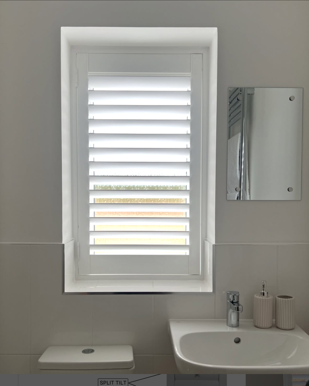A bathroom with a window covered by white horizontal blinds, a mirror on the wall to the right of the window, a white sink with a silver faucet below the mirror, and a white toilet tank at the bottom of the image. Two beige containers with a pump dis