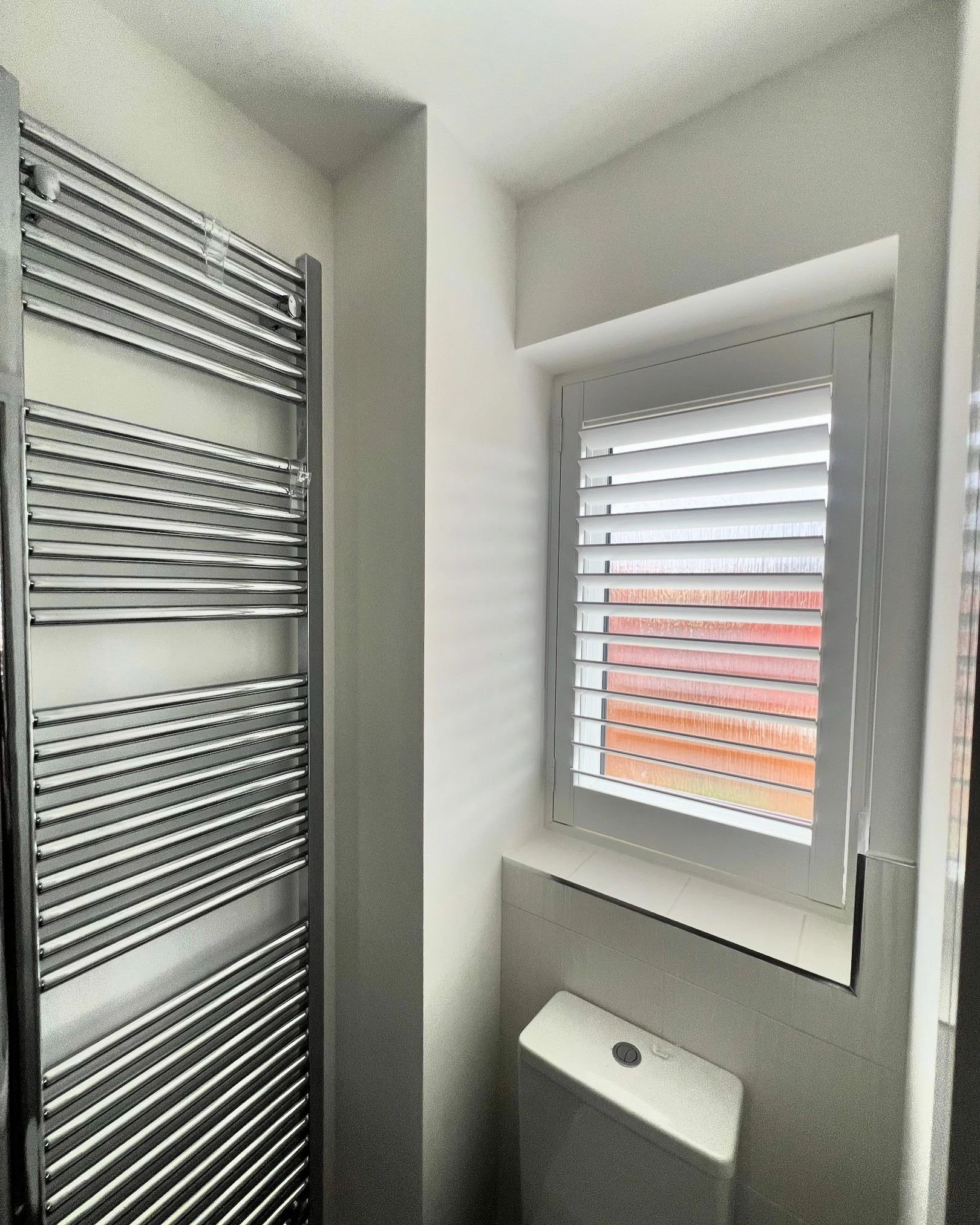 A small bathroom with a window that has white horizontal blinds and a white radiator on the wall.