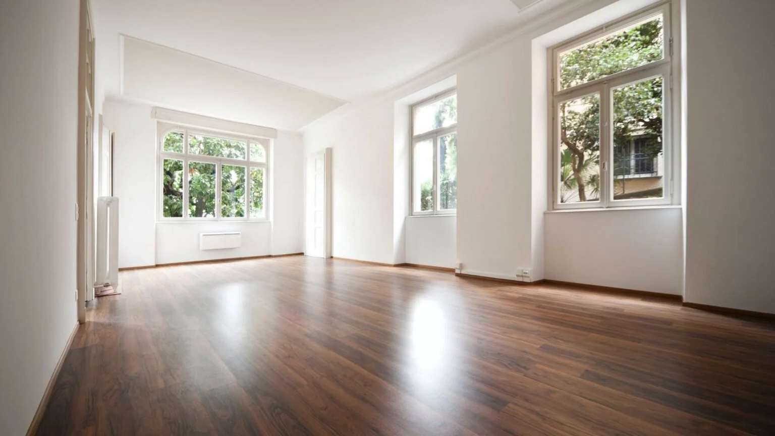 Empty living room with white walls, large windows, and wooden floors.