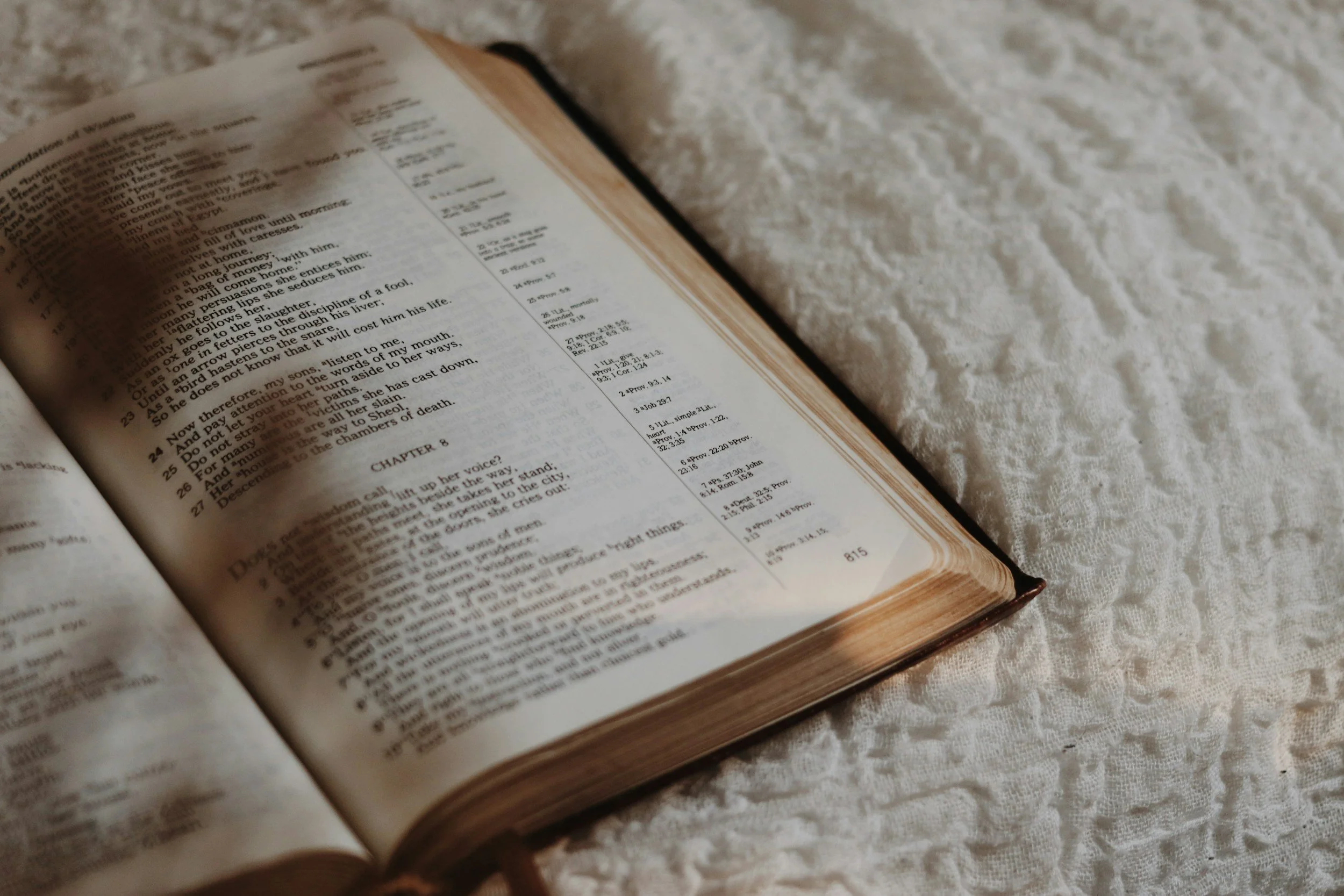 An open Bible lying on a white textured fabric surface.