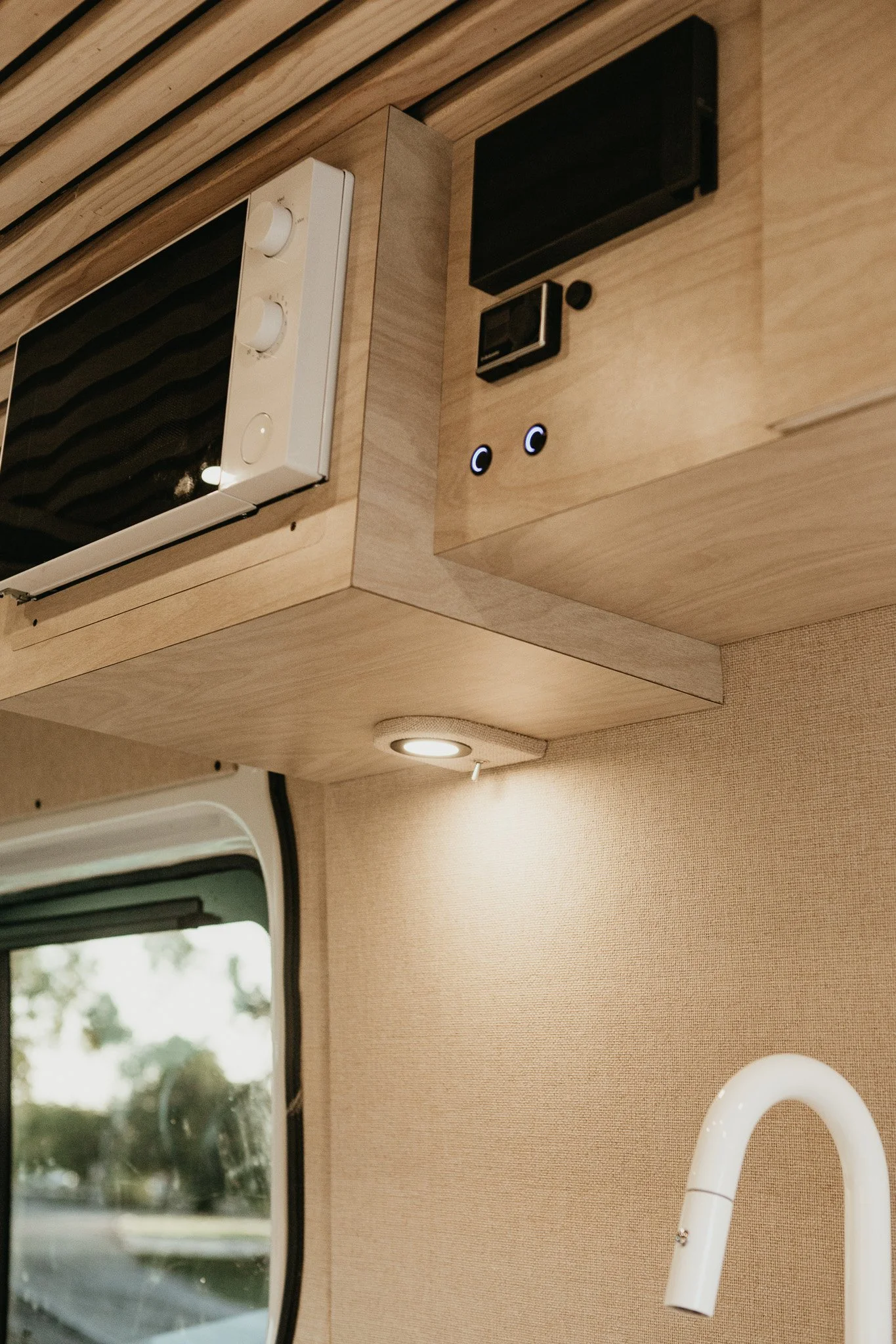 Bespoke camper van storage solutions featuring flush-latched overhead cabinets, and microwave.