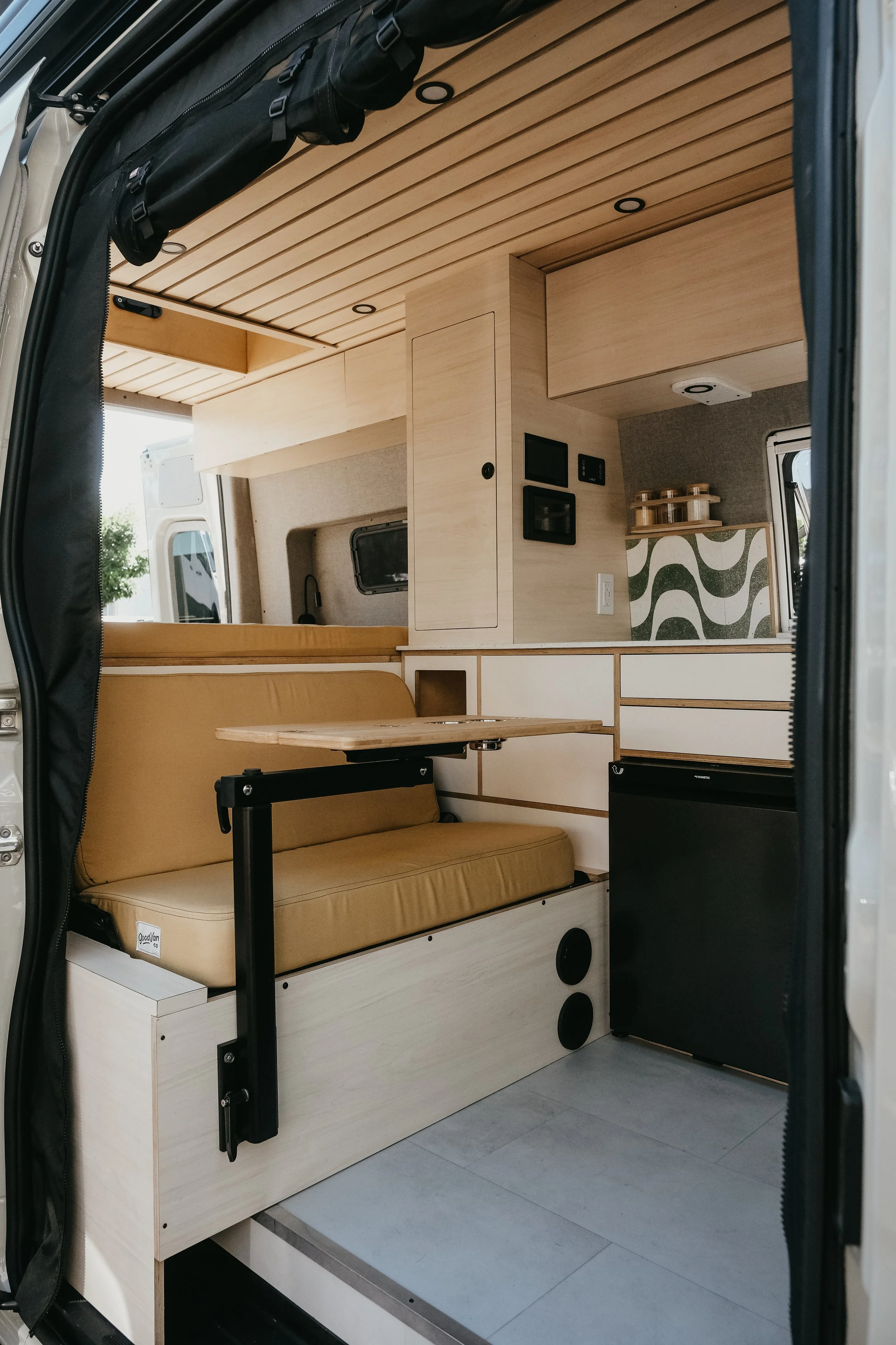 Side view of a custom interior build inside a mercedes sprinter van with bench seating, modular table, wooden cabinets, and kitchen storage