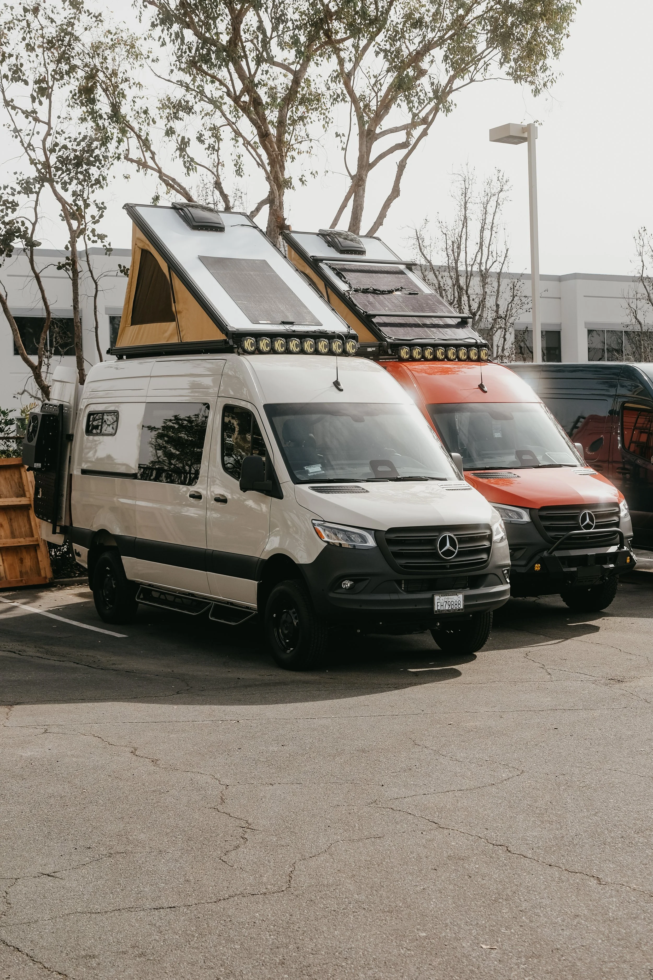 Tan and red Mercedes sprinter vans both with super pacific roof top tents in a parking lot