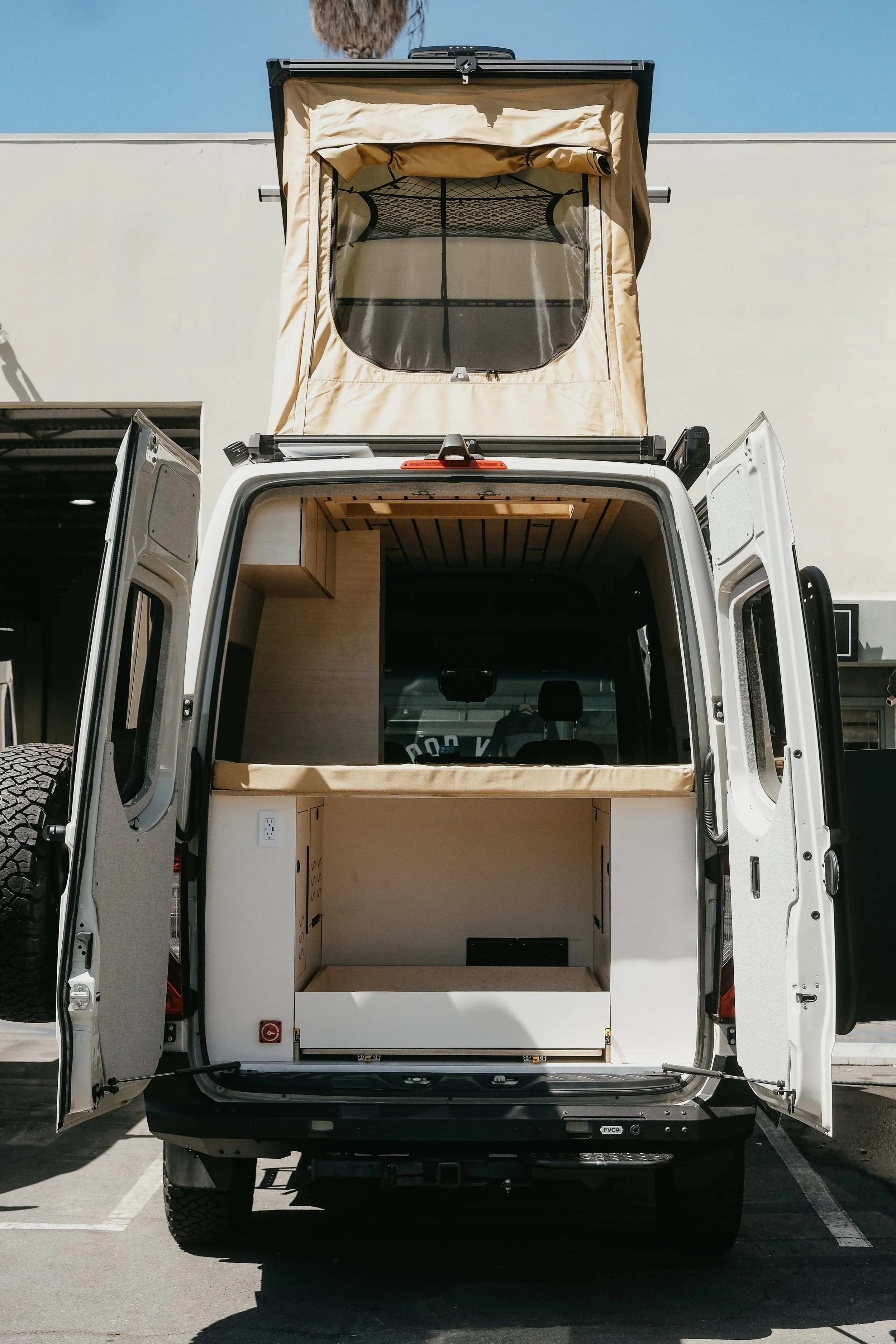 Rear view of a Mercedes van build outs with the two back doors open with a custom interior build and a super pacific roof top tent