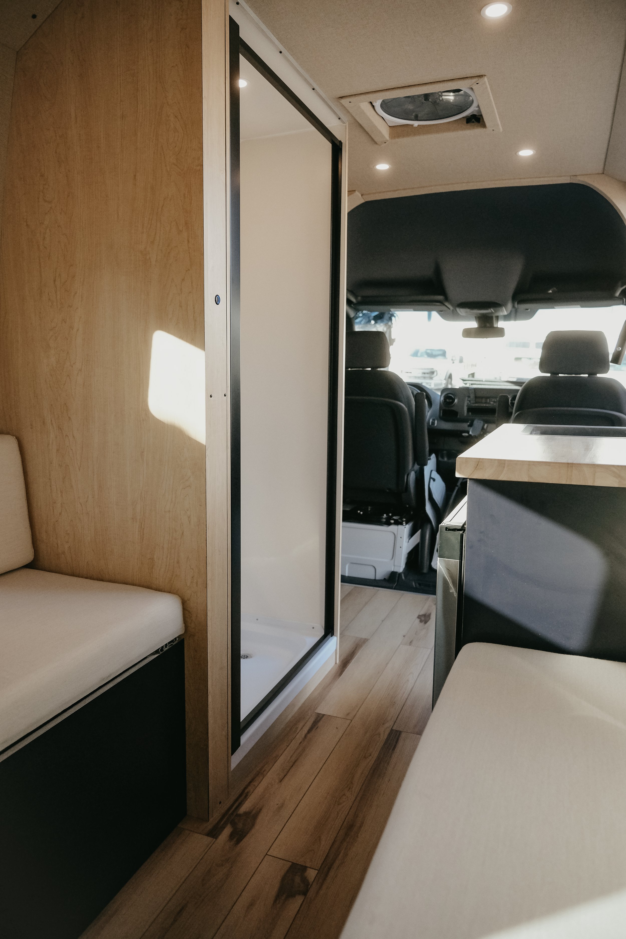 Bespoke sprinter van interior build featuring bench seating, kitchen area, and shower. 
