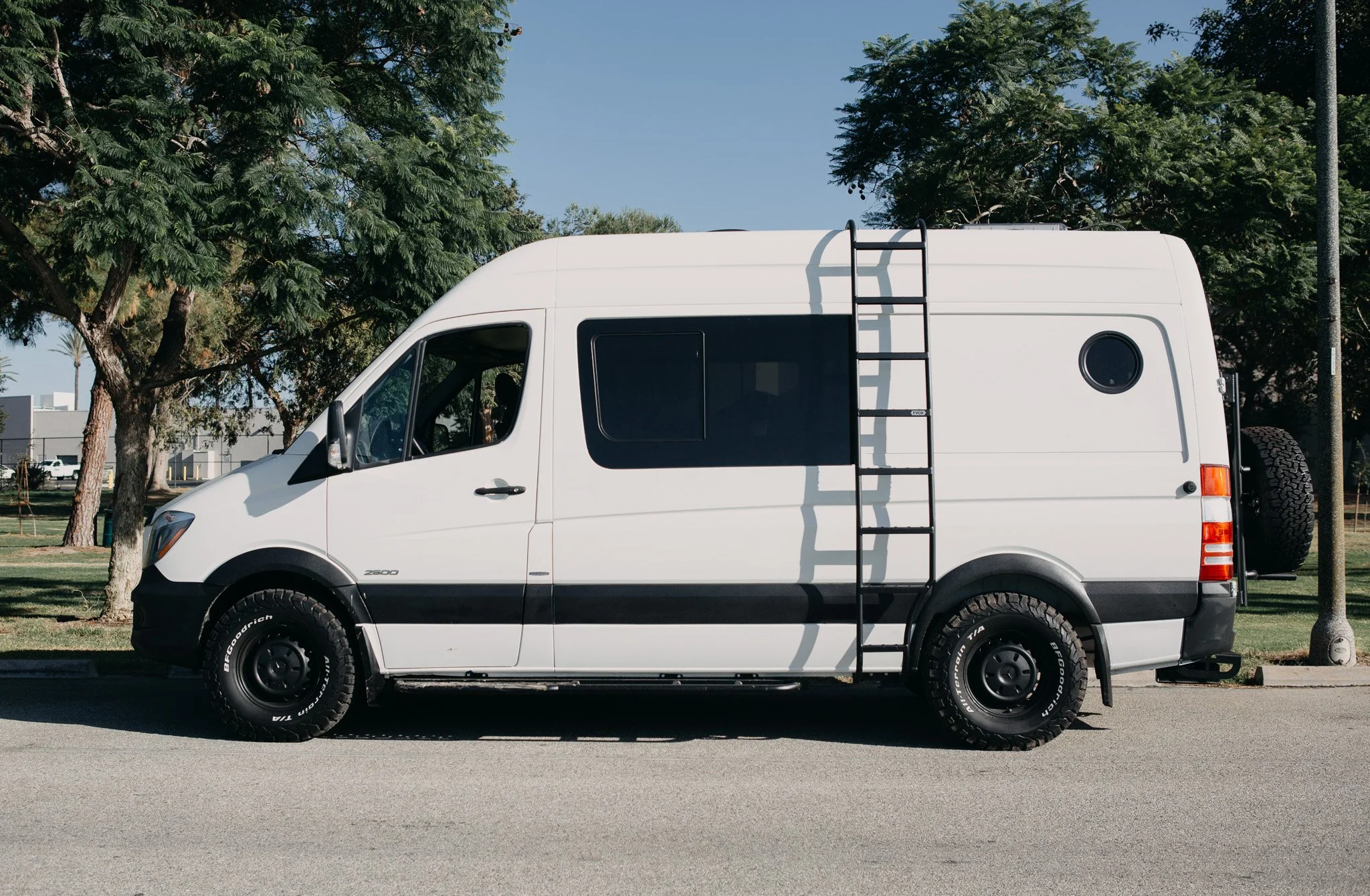 Side view of a Mercedes sprinter van with a side ladder, lift kit, and new tires