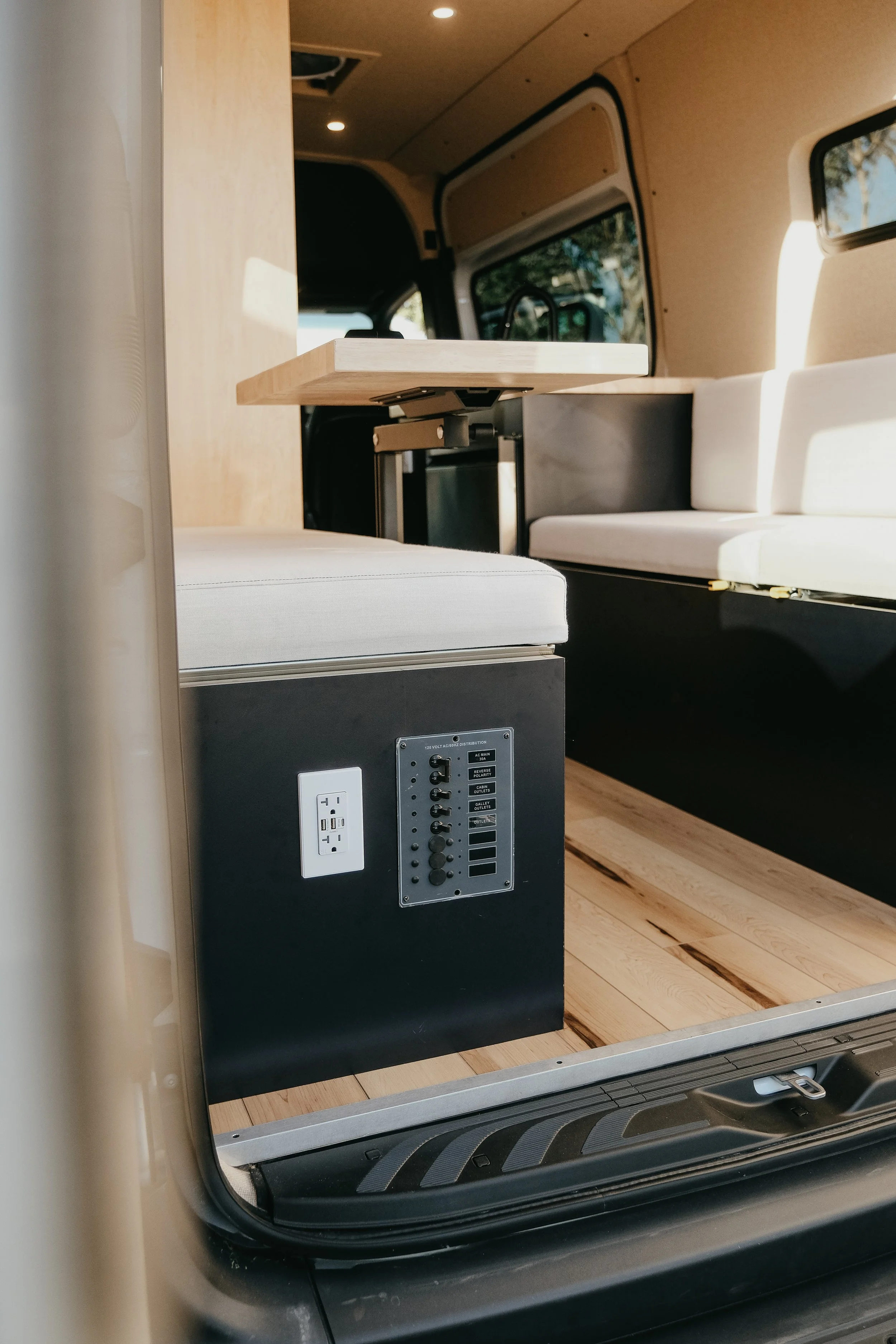 Rear view of an interior custom build for mercedes sprinter van, featuring bench seating, table, and outlets. 