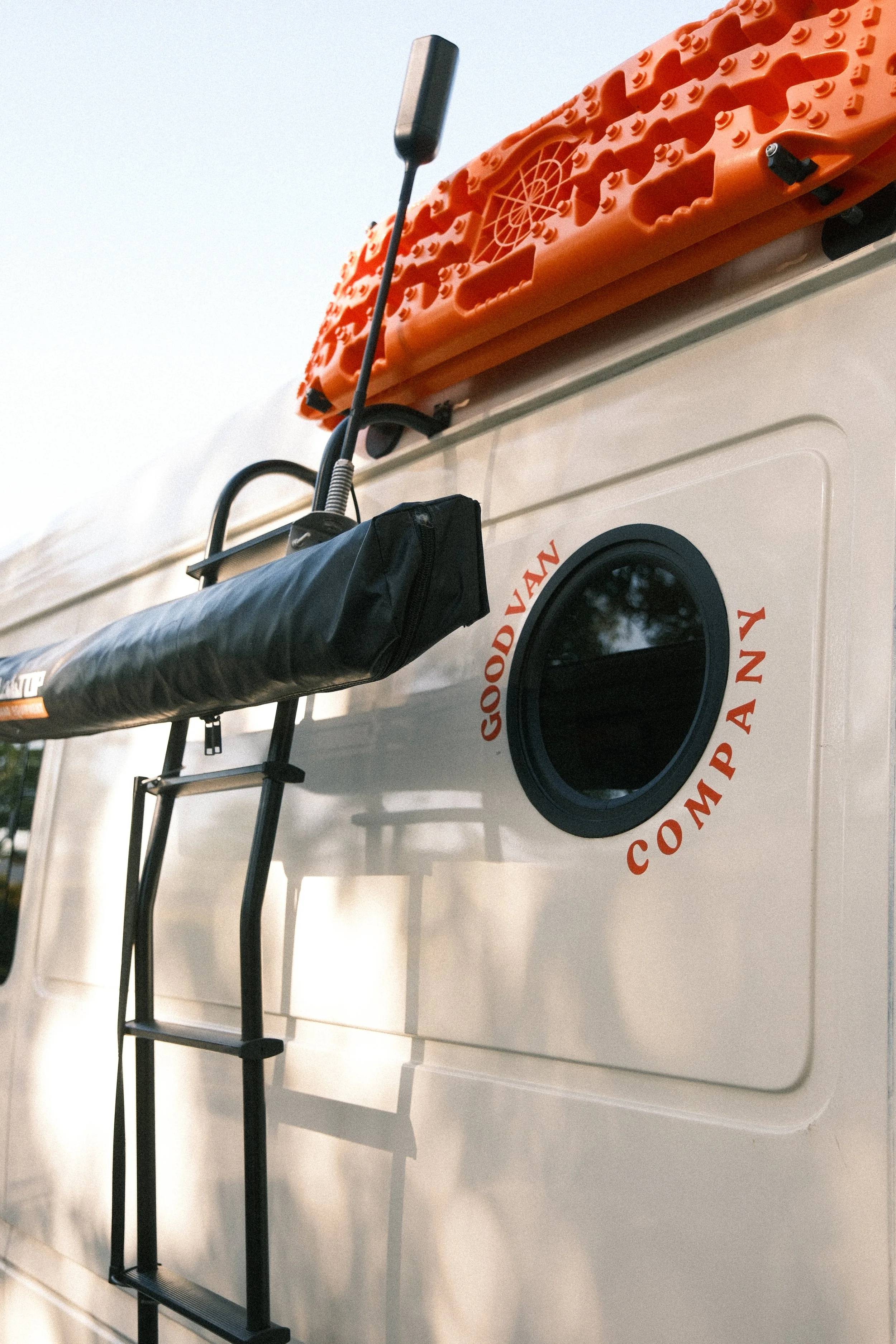 Side view of a mercedes sprinter van with custom circular window, side ladder, and surf poles holding up kayak