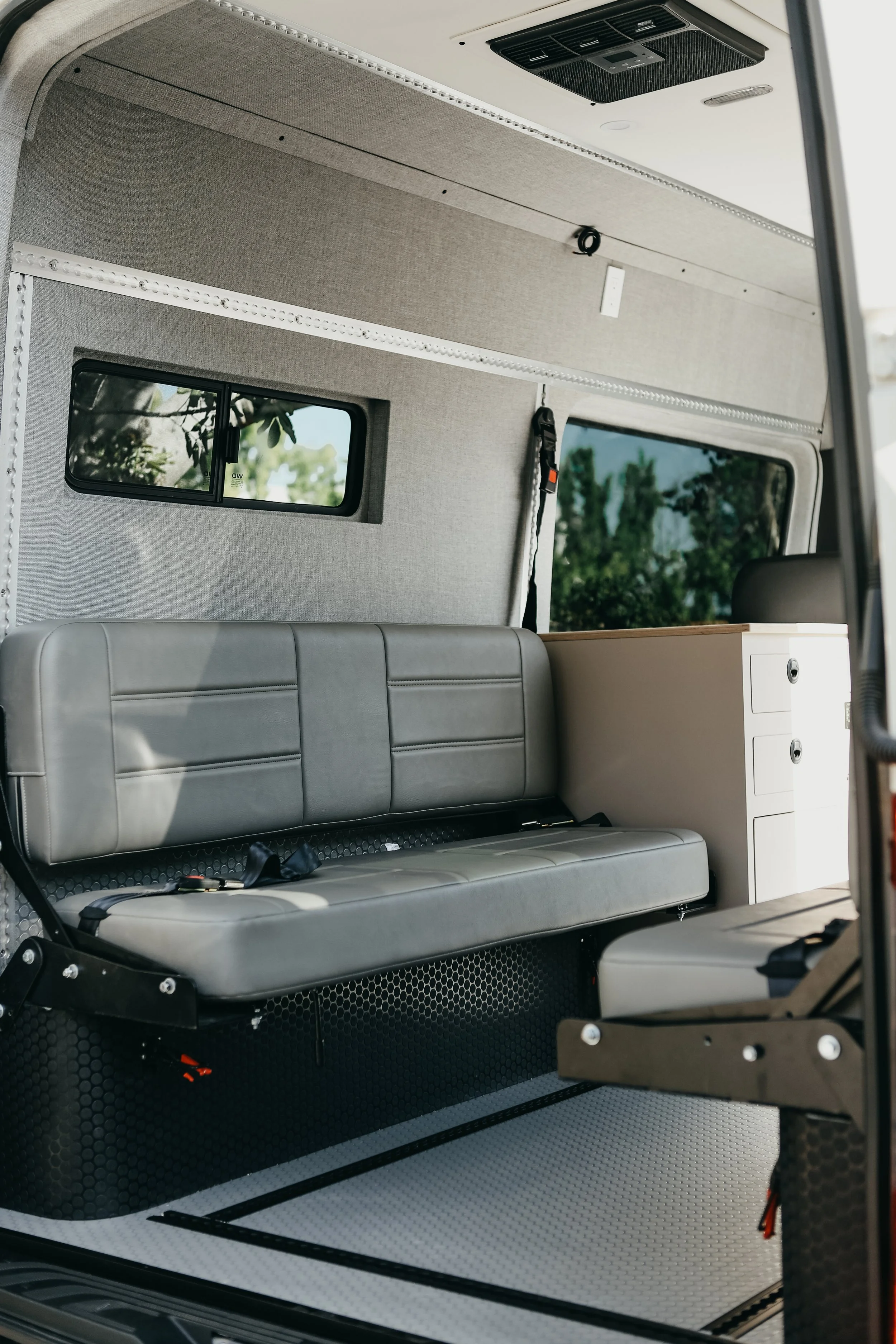 Contemporary Sprinter camper van living area featuring a custom sofa with built-in seatbelts and storage.