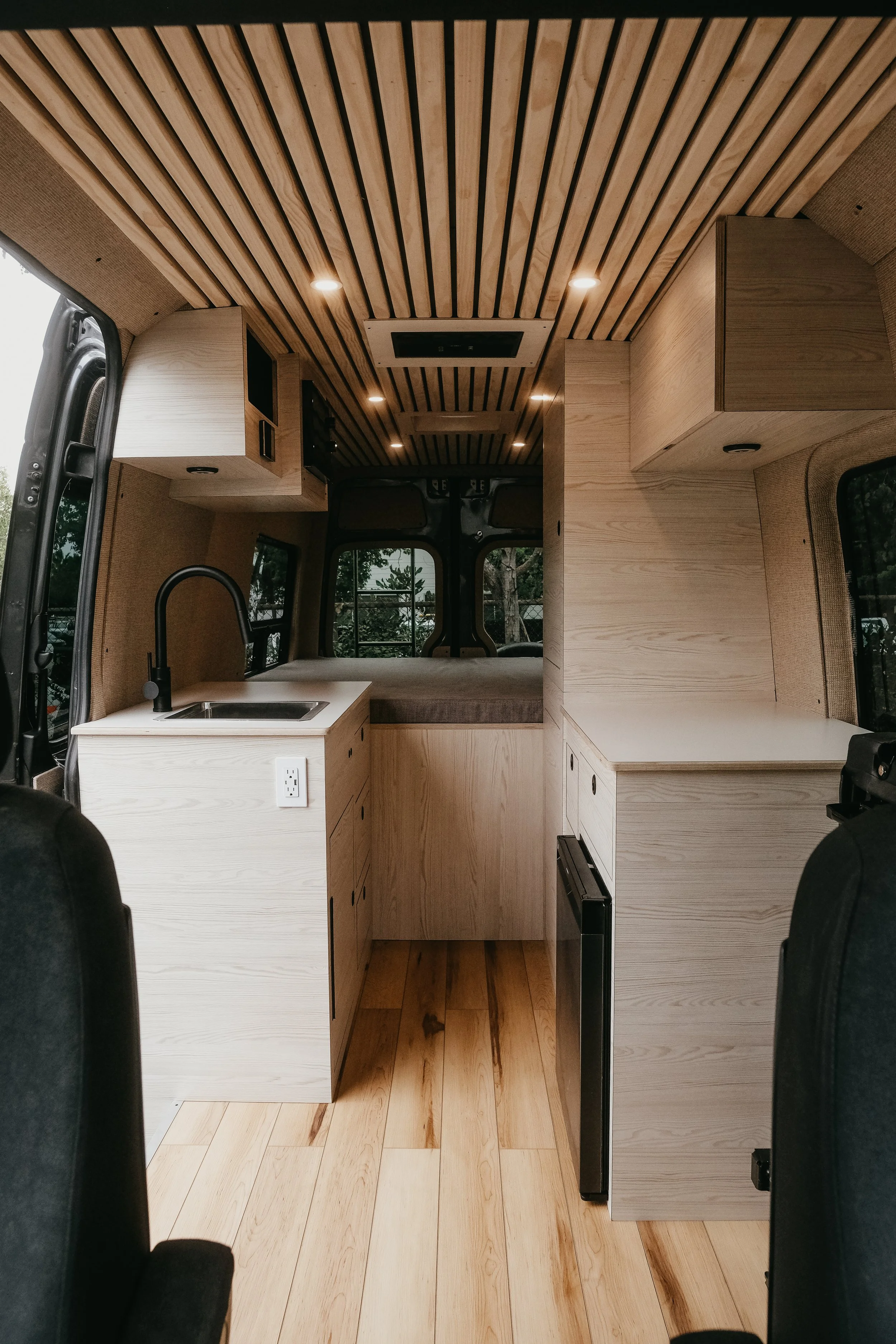 Architecturally refined Sprinter kitchen layout featuring integrated premium appliances and bed at the end of the cabin 