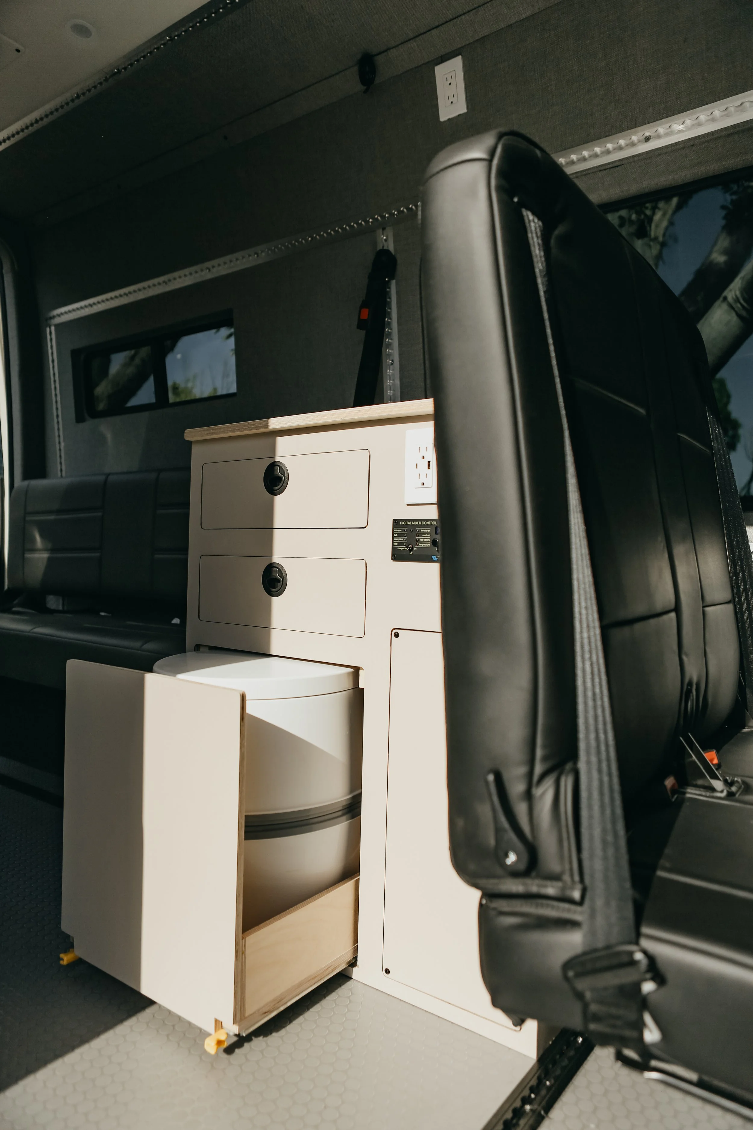 Bespoke camper van storage solutions featuring flush-latched overhead cabinets and hidden toilet .