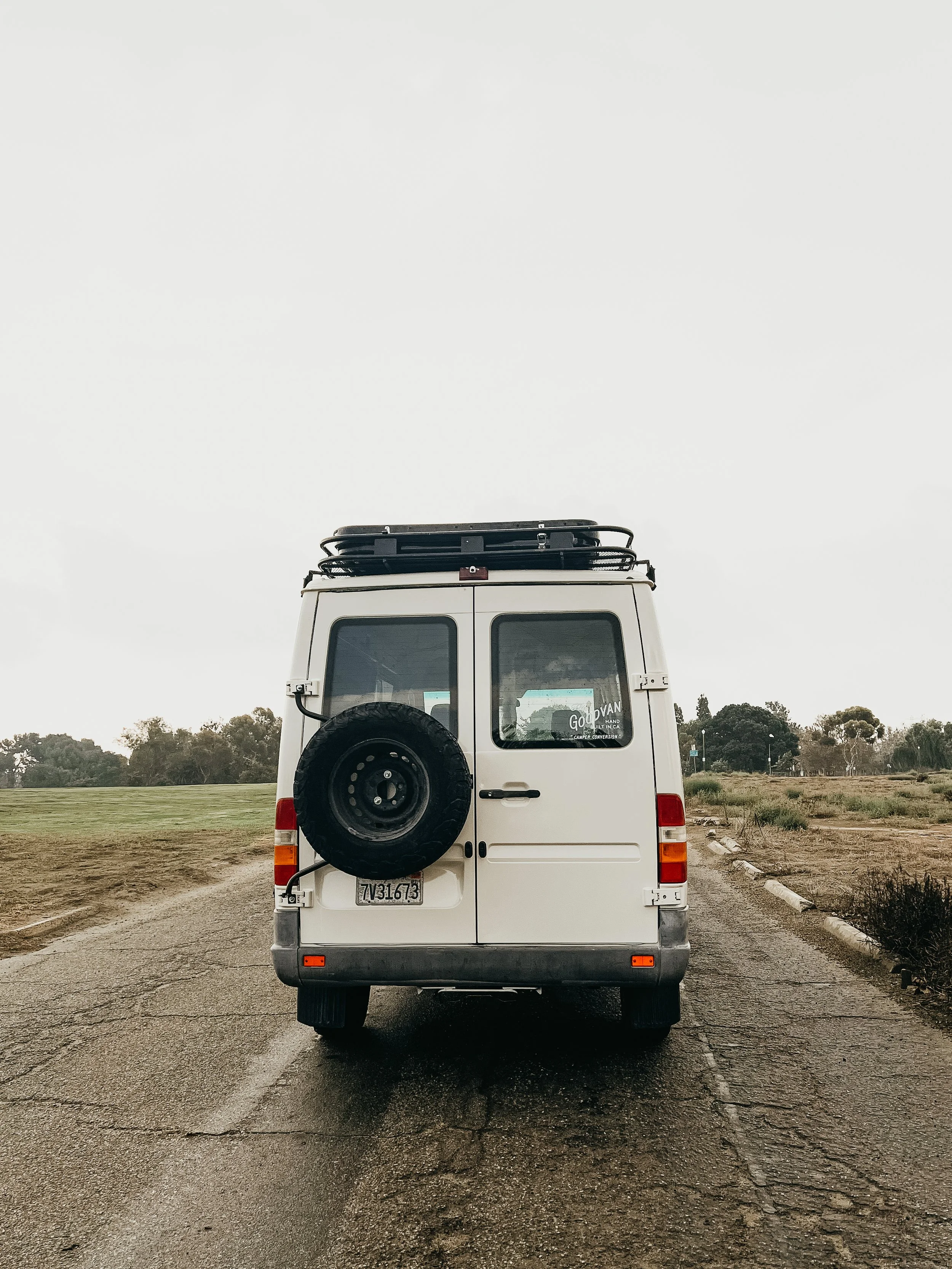 Rear of customized van for camping on the road with tire carrier and closed roof top tent
