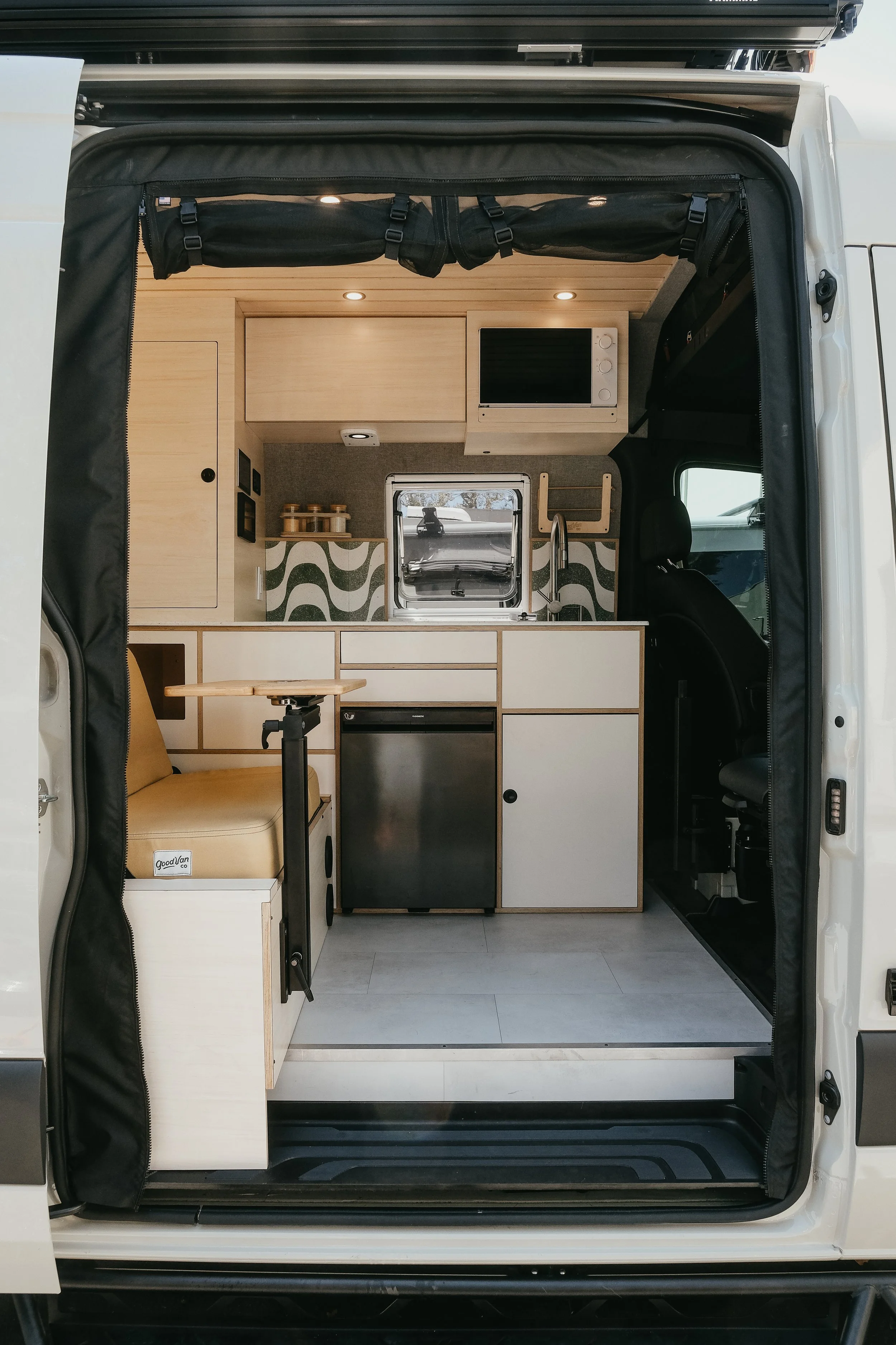Side shot of a custom interior build for Mercedes sprinter van featuring custom cabinets, sink, bench seating with modular table and microwave 