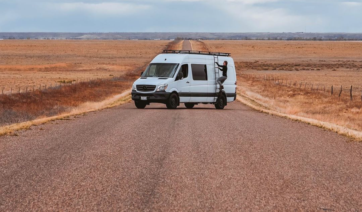 Custom sprinter van camper in the middle of the road with person climbing up side ladder
